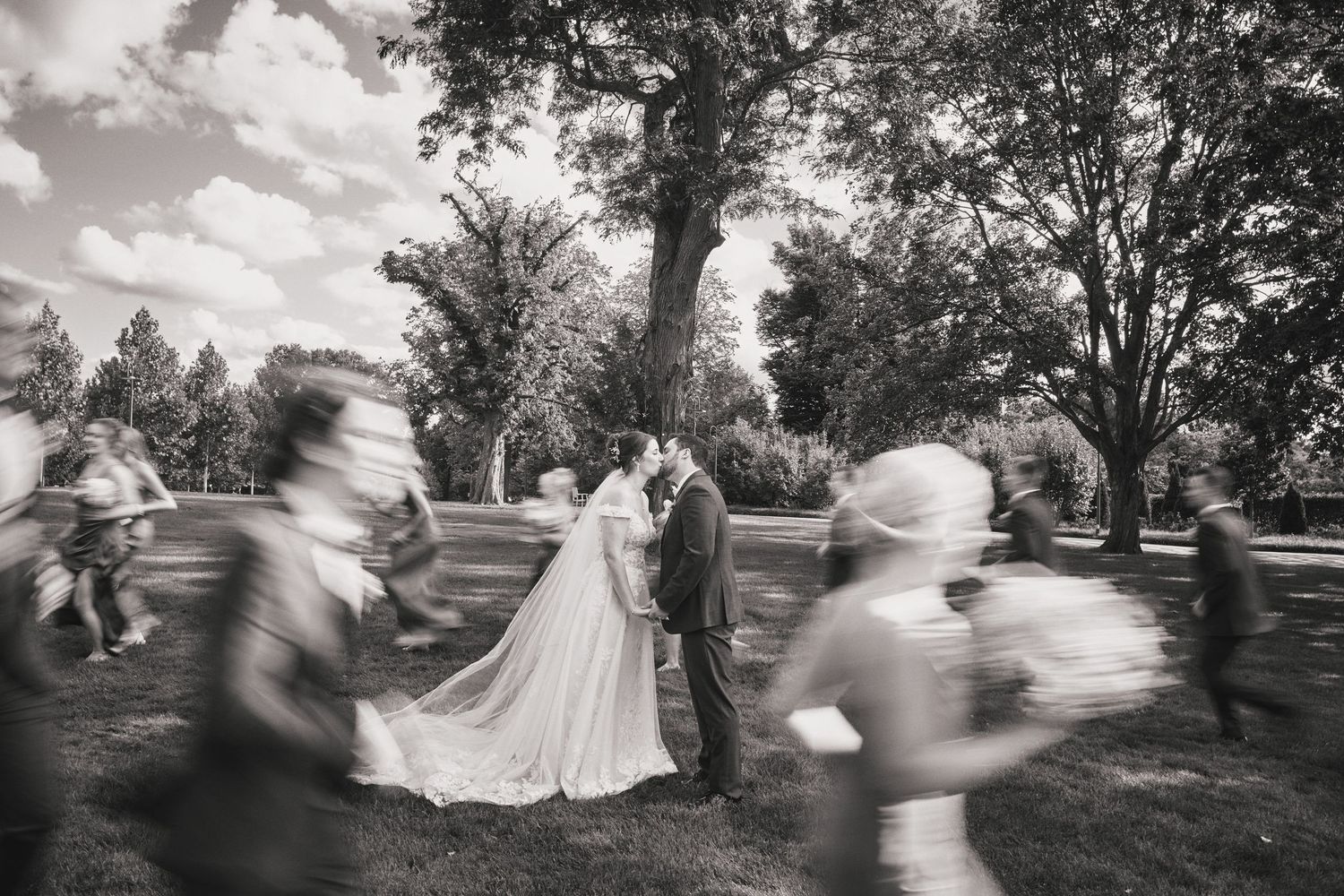 Panoramic black and white wedding photo showing silhouettes of people dancing in a garden setting.