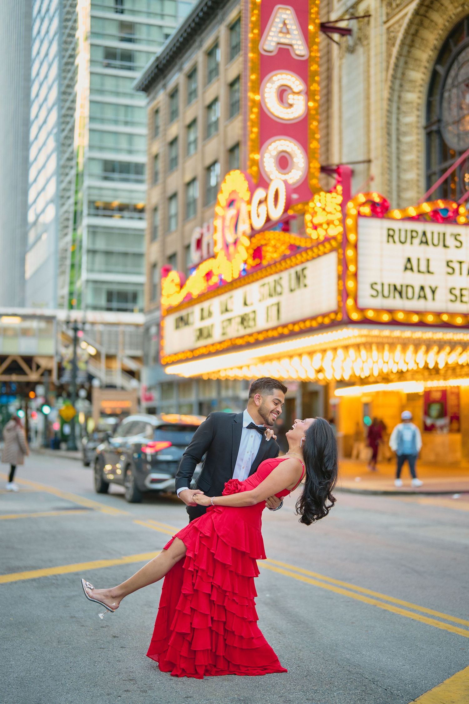 A couple poses romantically in front of the illuminated Chicago Theatre marquee displaying RuPaul's show.