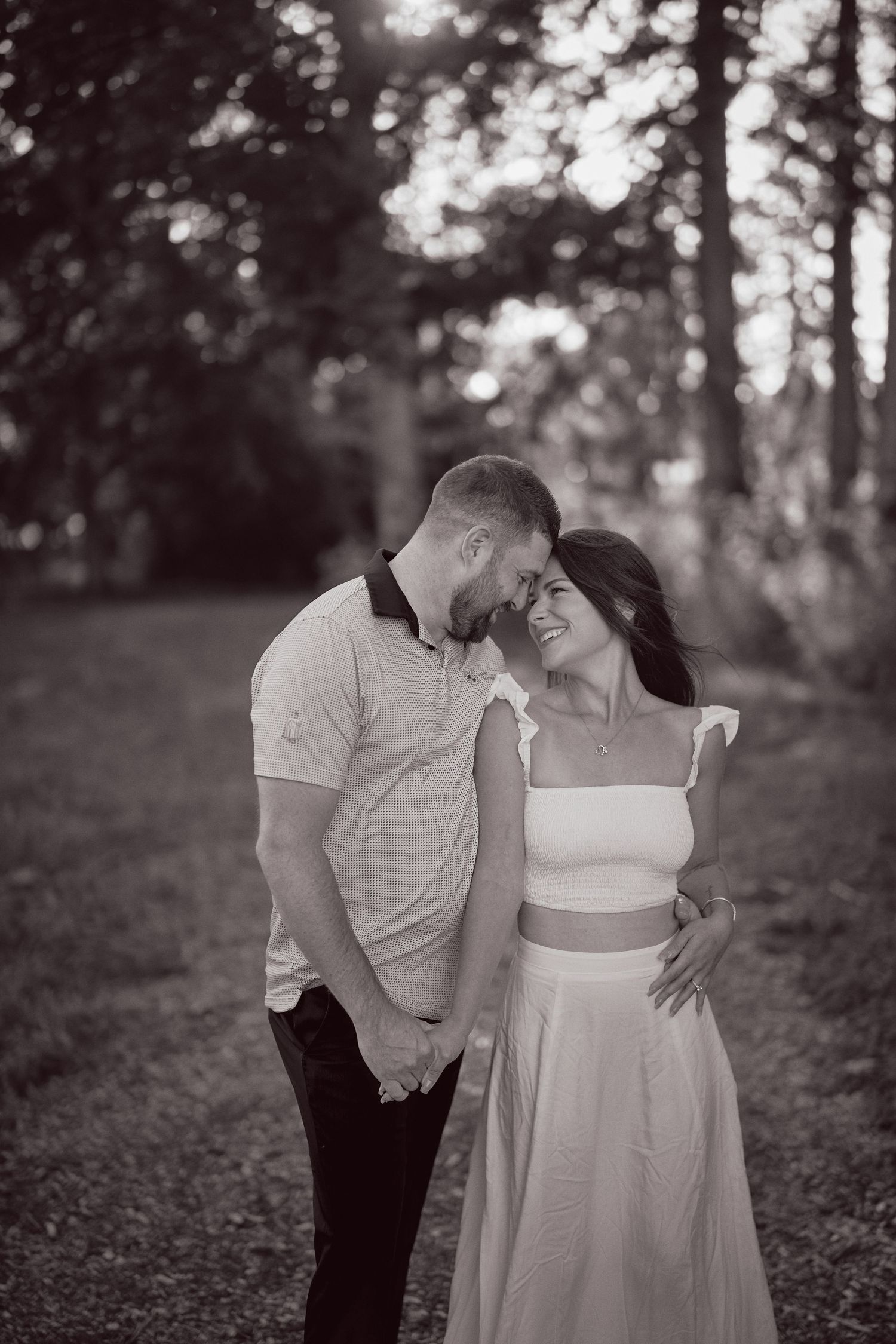 A romantic black and white photograph of a couple sharing an intimate moment in a sunlit forest.