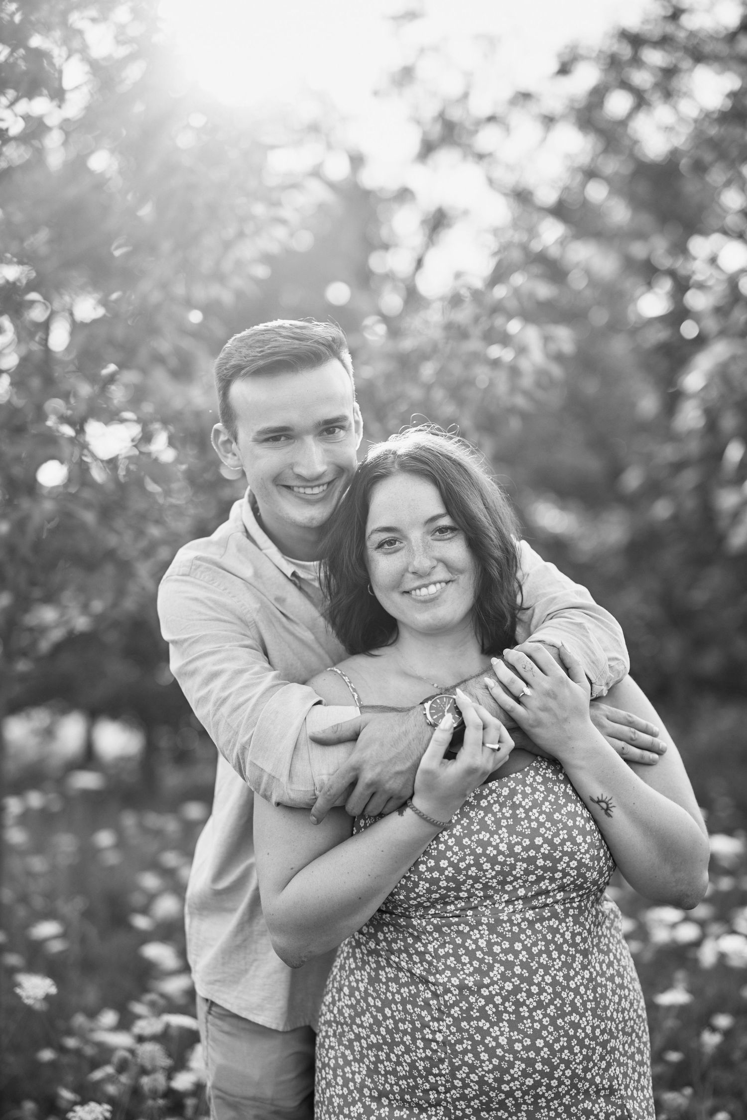 A romantic black and white photo showing a loving couple embracing outdoors with bokeh lighting effects in the background.