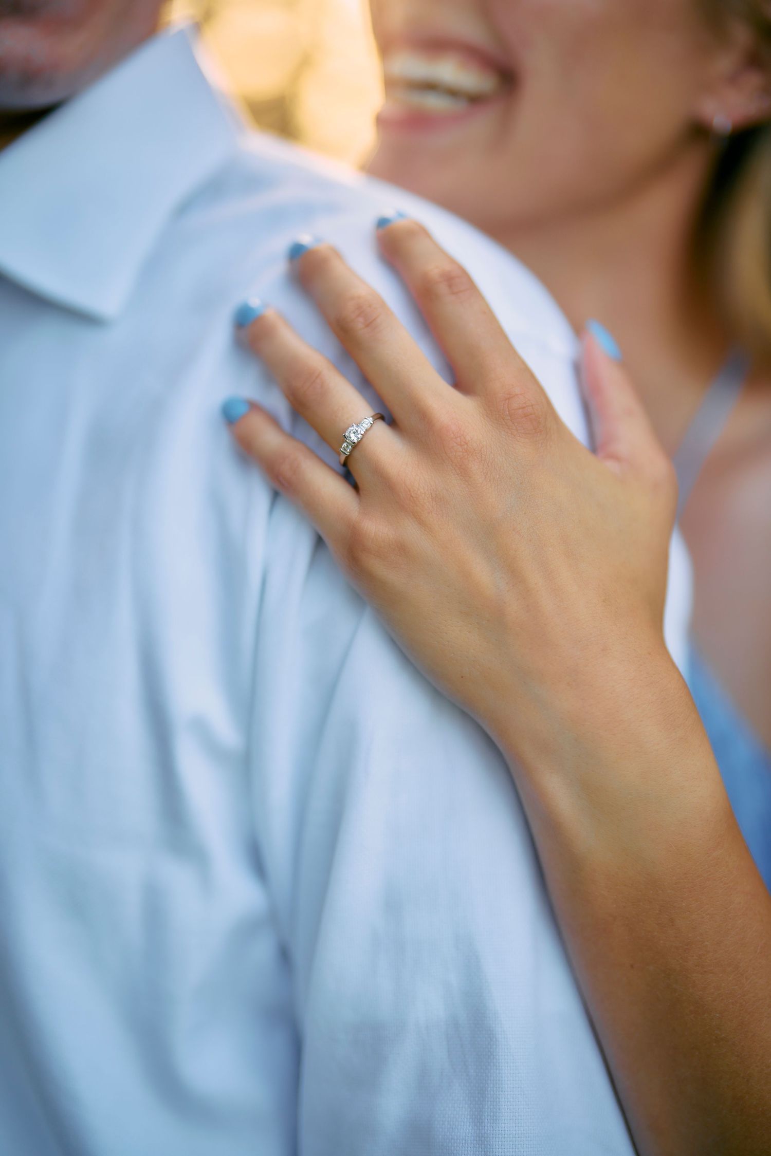 A hand wearing a wedding band rests gently on a light blue dress shirt in an intimate pose.