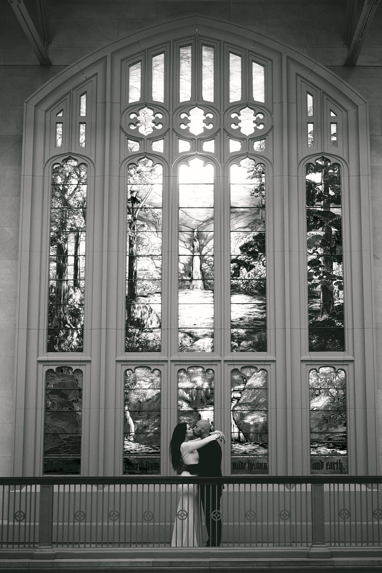 A silhouetted figure stands against a large Gothic church window with ornate stained glass panels in black and white.