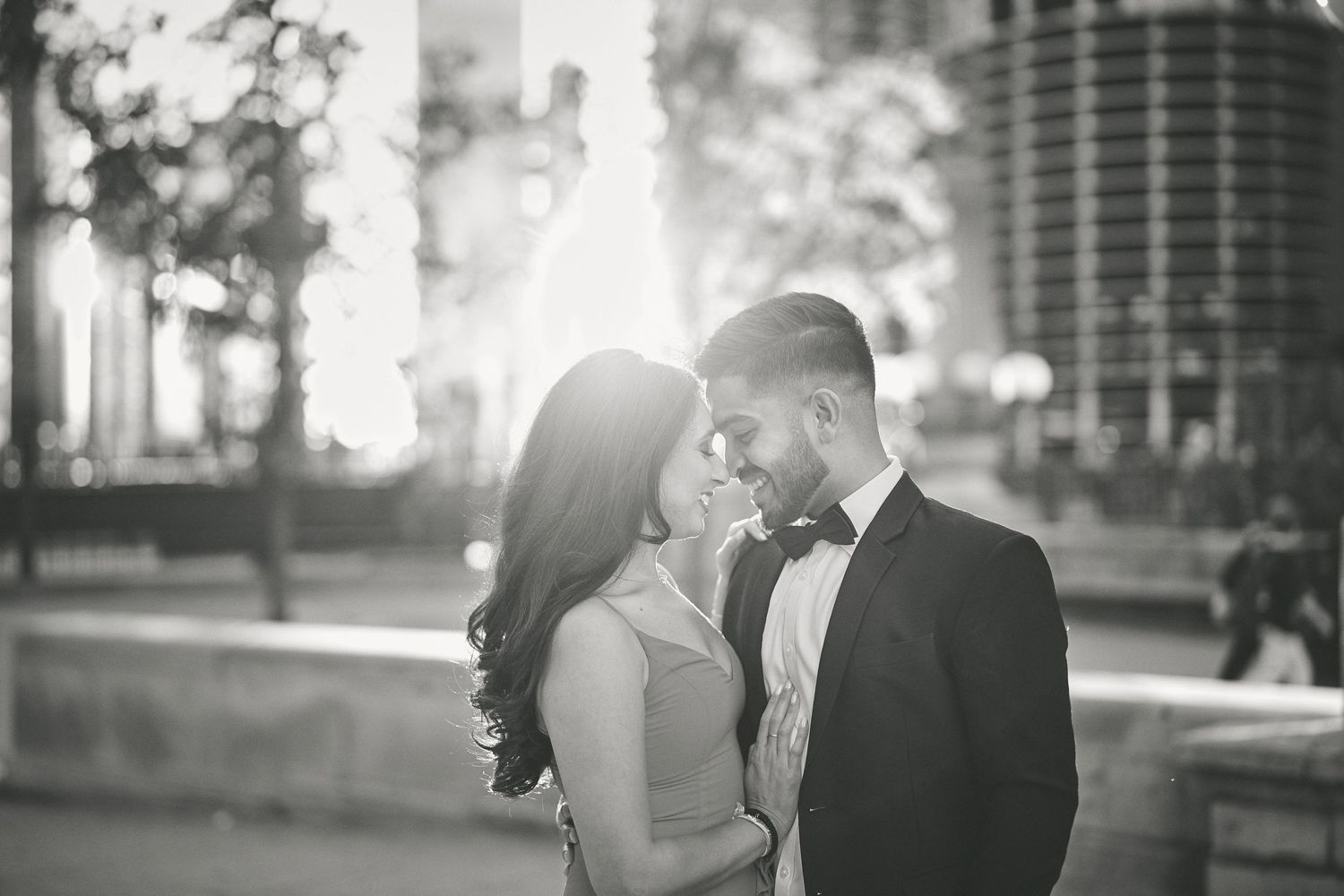 A romantic black and white photograph of a couple in formal attire sharing an intimate moment outdoors at sunset.