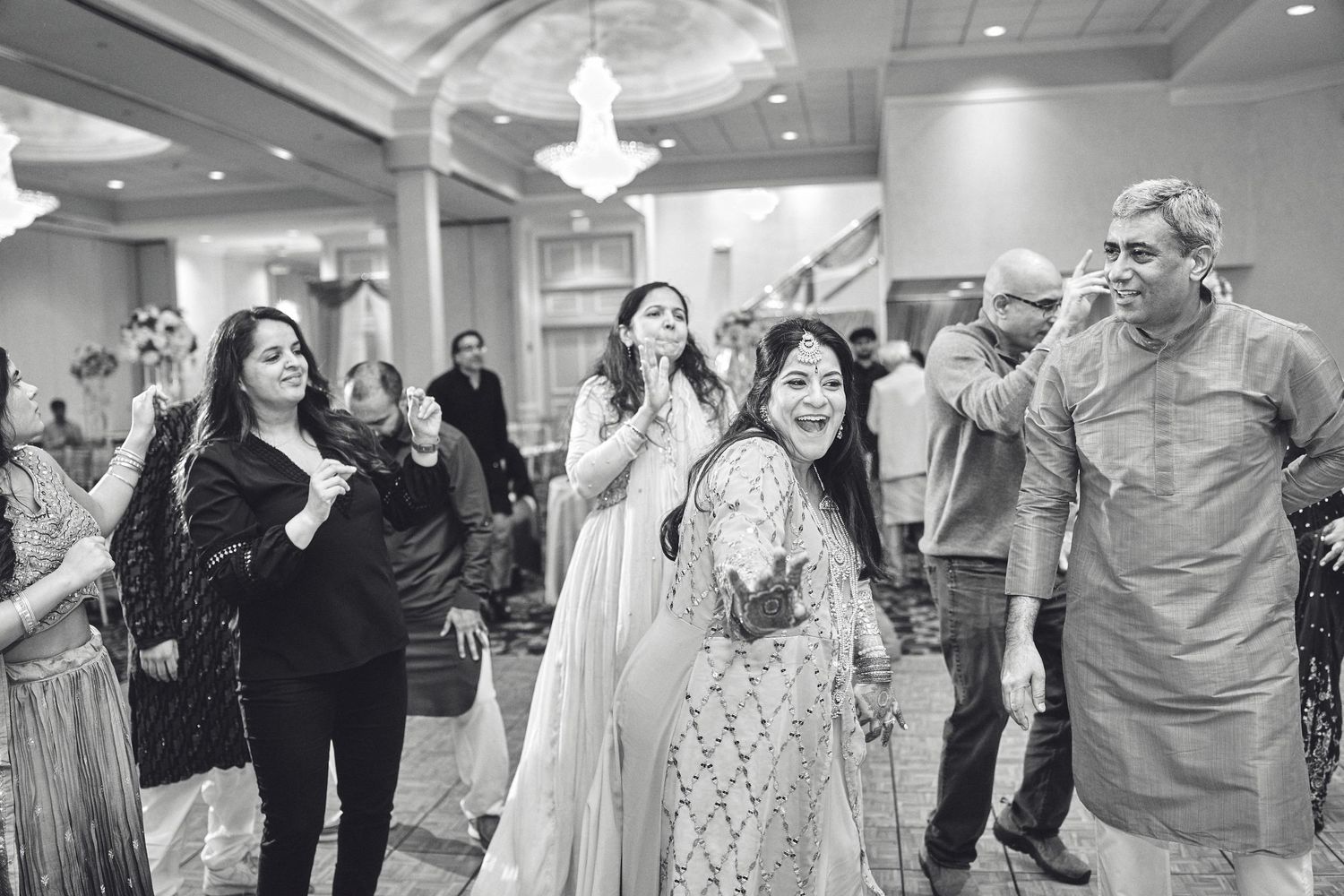A group of people celebrate joyfully at an elegant indoor event with chandelier lighting and festive atmosphere.