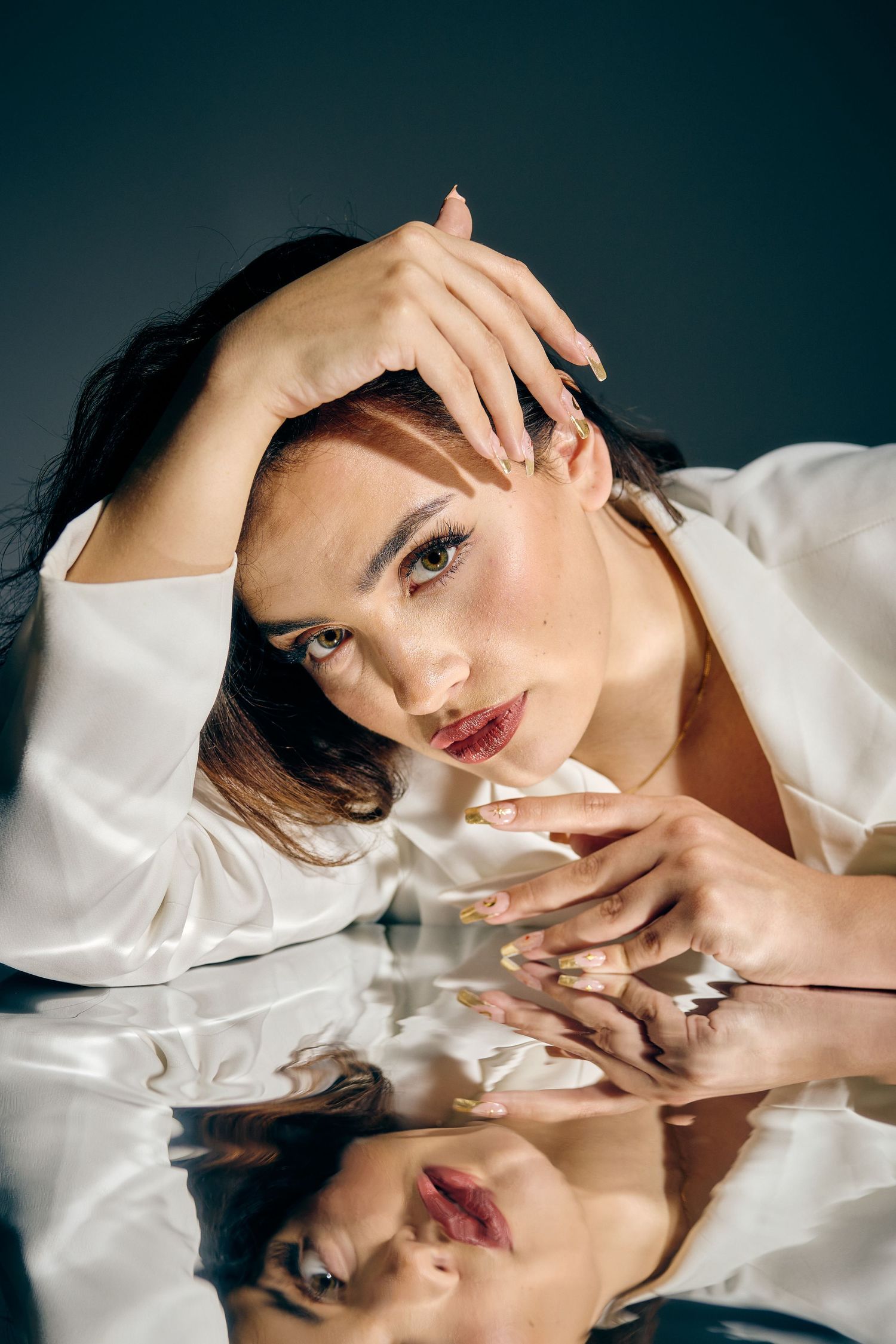 Glamorous beauty portrait with mirror reflection showing dramatic makeup and silk blouse.