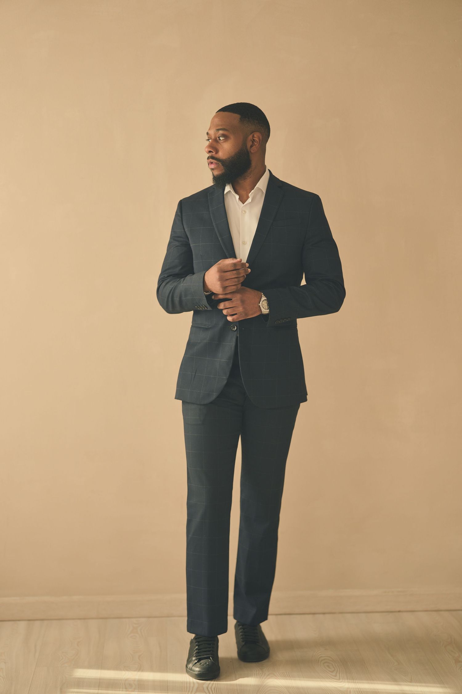 Professional portrait in formal suit adjusting cufflinks against neutral background.