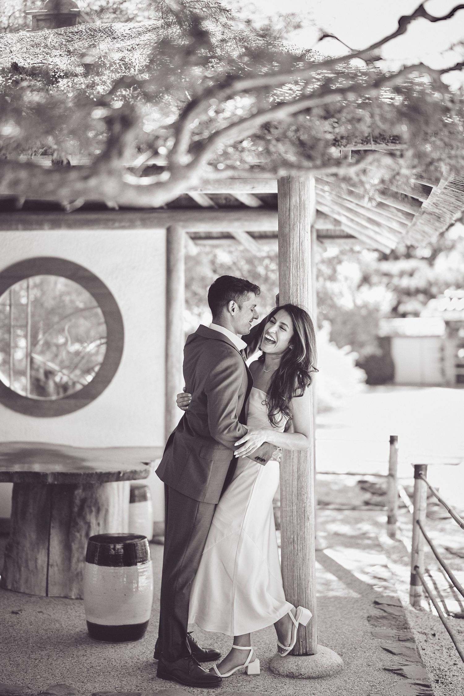 A romantic black and white portrait of a couple embracing under a traditional Japanese garden structure.