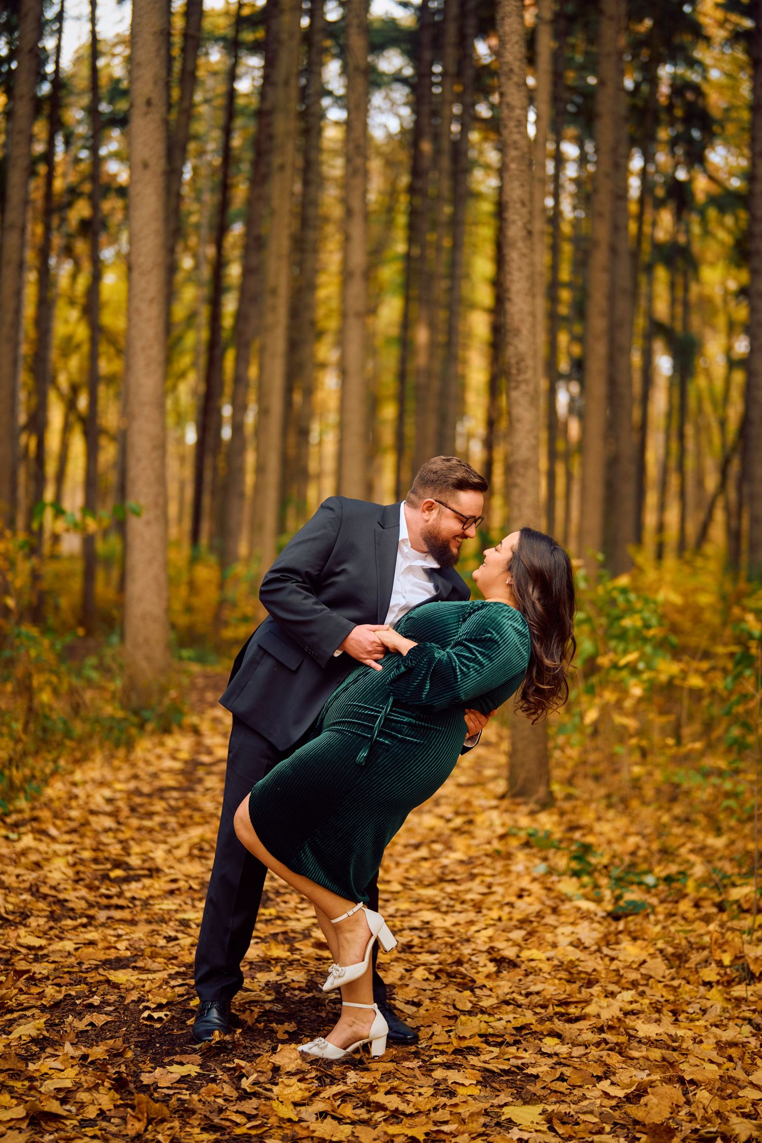 A romantic autumn forest scene with a couple sharing an intimate dance pose among fallen leaves and tall trees.