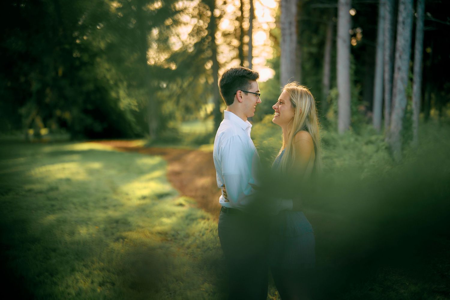 A romantic couple shares an intimate moment in a sunlit forest setting during golden hour.