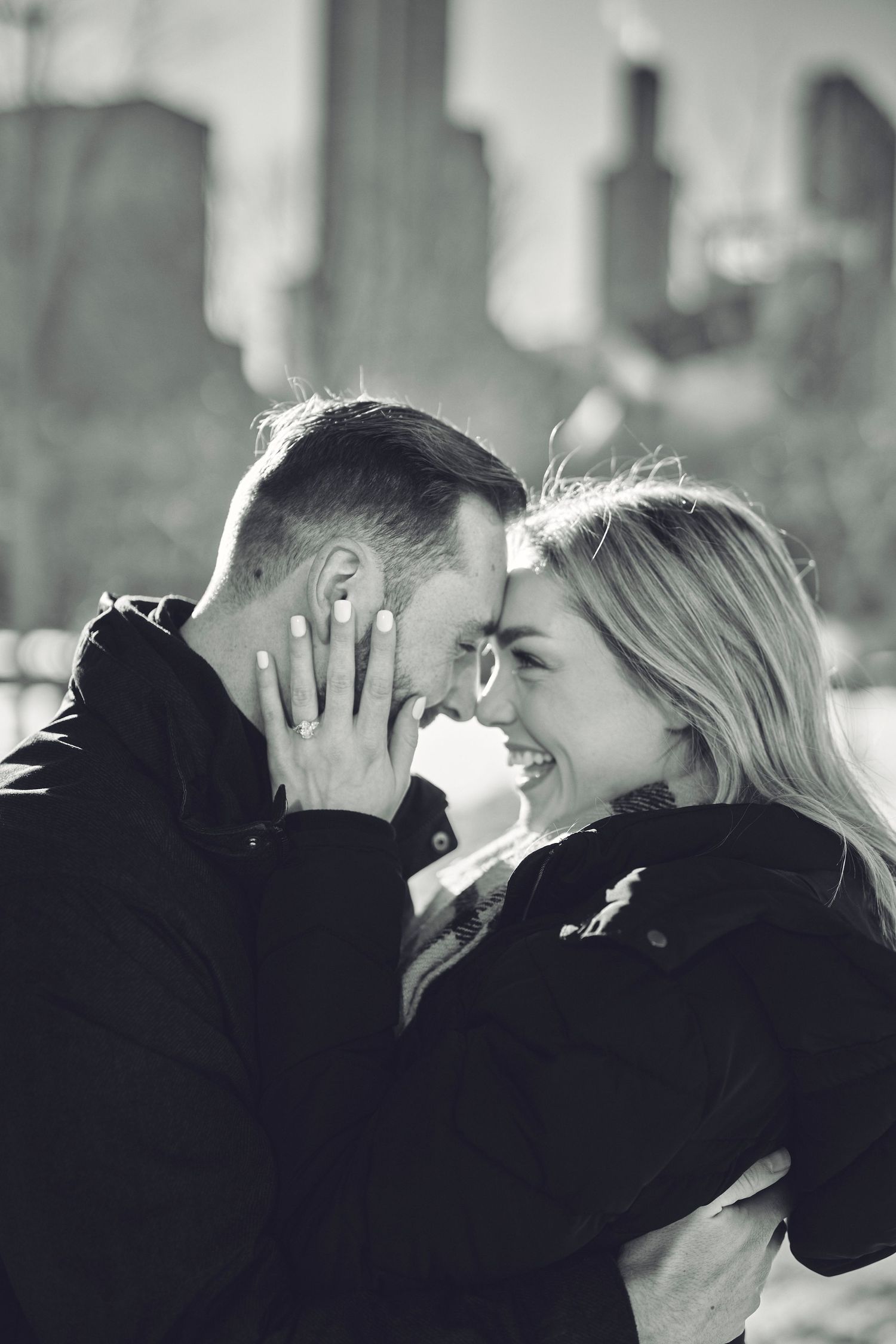 Black and white romantic moment between couple sharing an intimate embrace with city skyline in background.