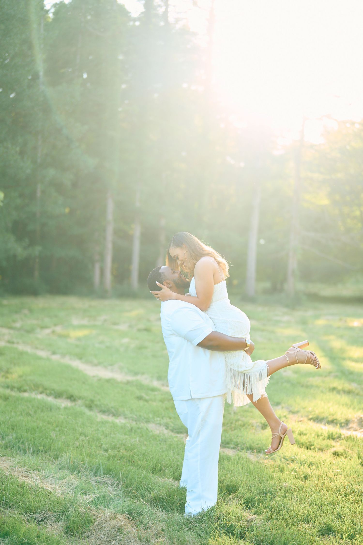 A romantic sunset engagement photo shows a couple embracing in an ethereal backlit meadow setting.