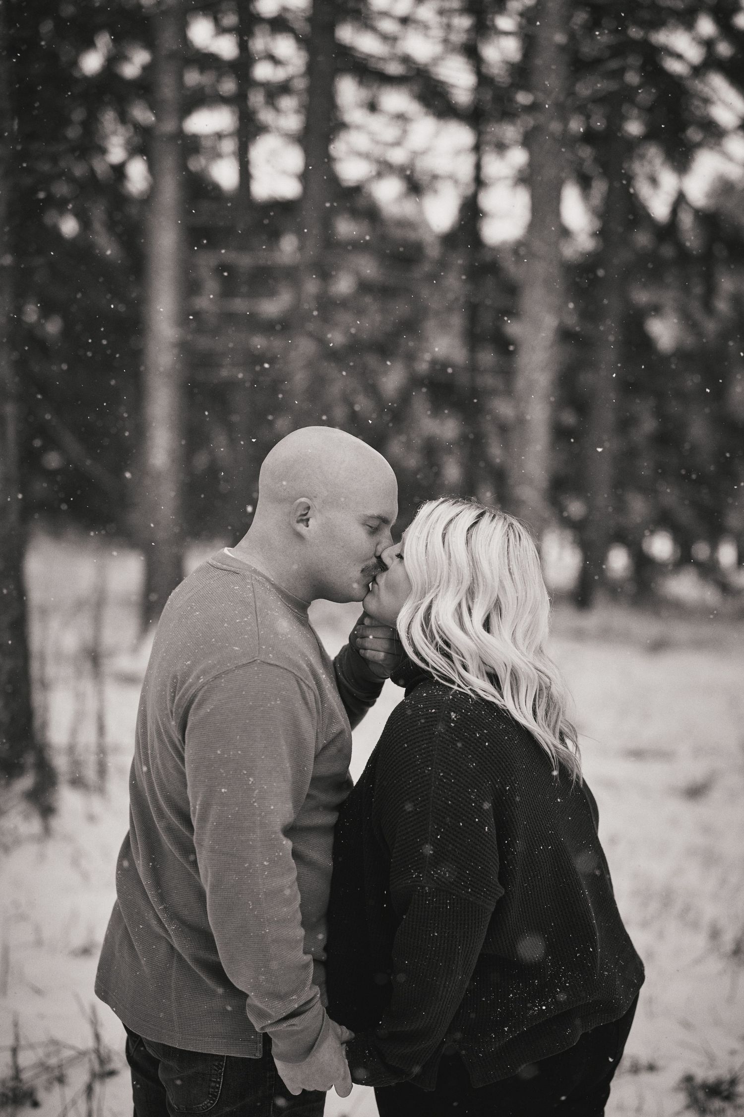 A romantic winter scene of a couple sharing an intimate moment in a snowy forest, captured in black and white.