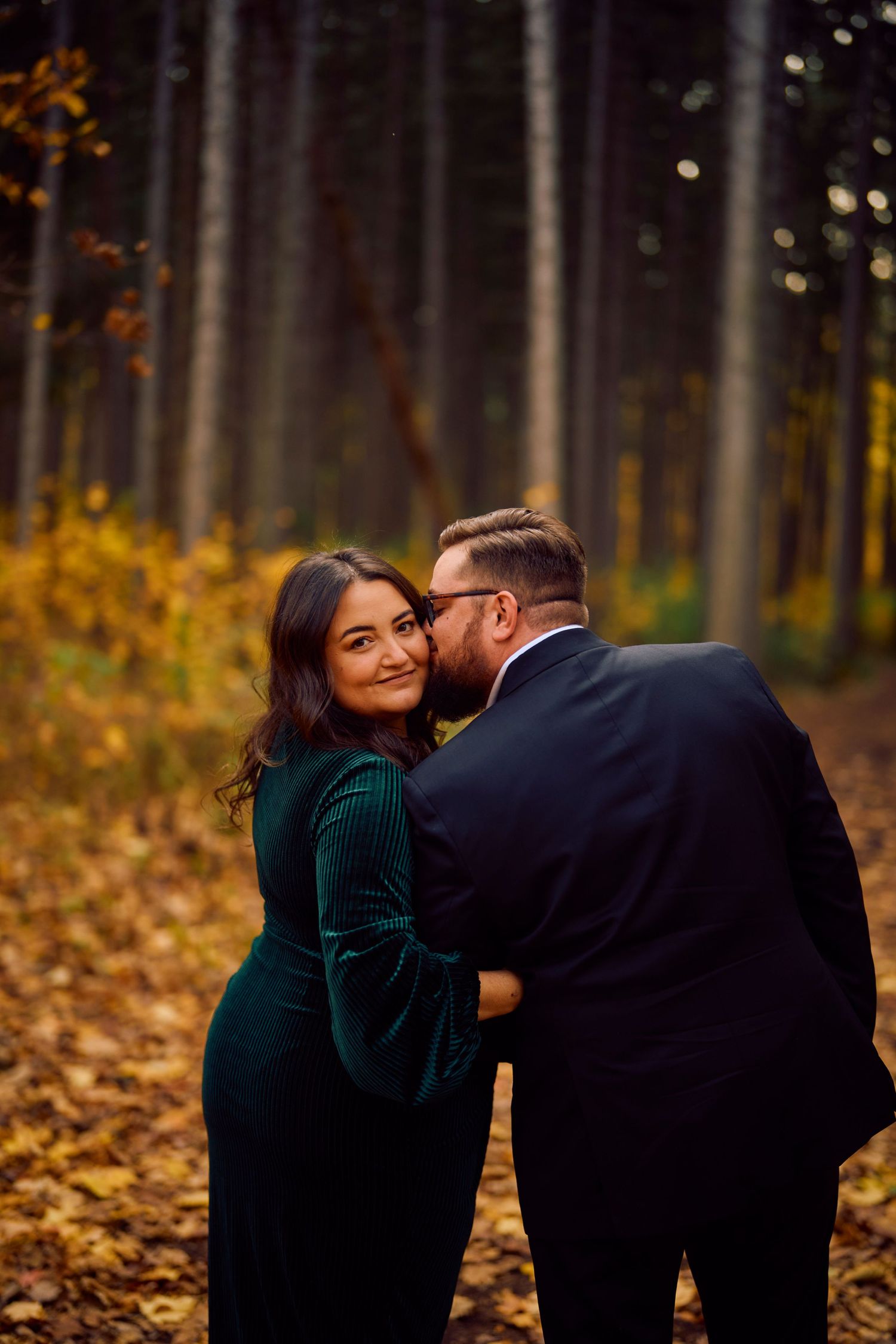 Romantic couple sharing an intimate moment in a forest with autumn leaves and warm lighting.