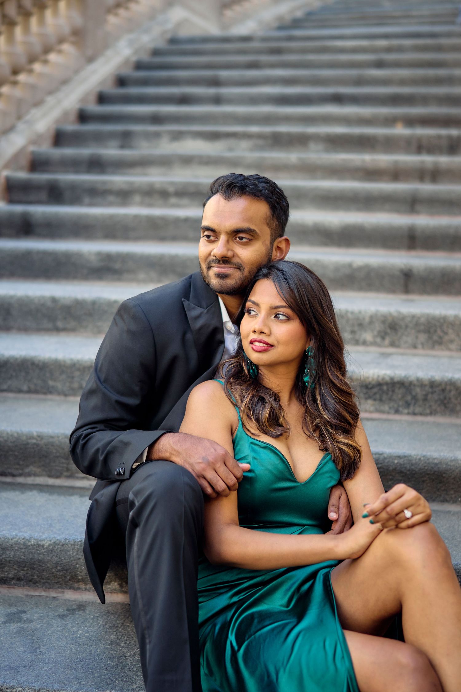 Elegant couple poses together on stone steps, with her in a green dress and him in a black suit.