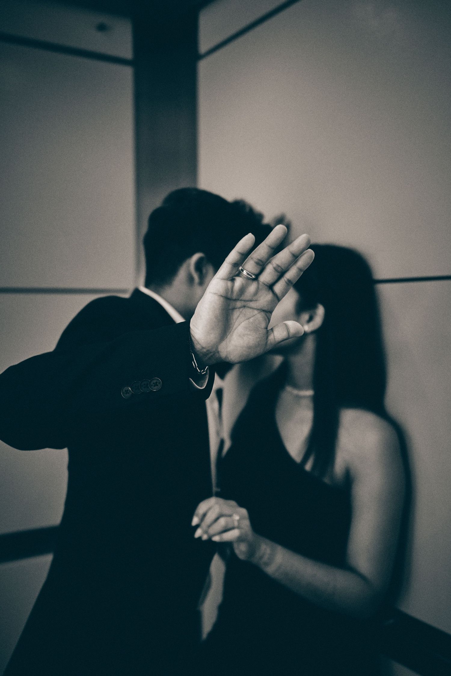 Black and white photo showing a raised hand blocking the view between two people in an intimate moment.