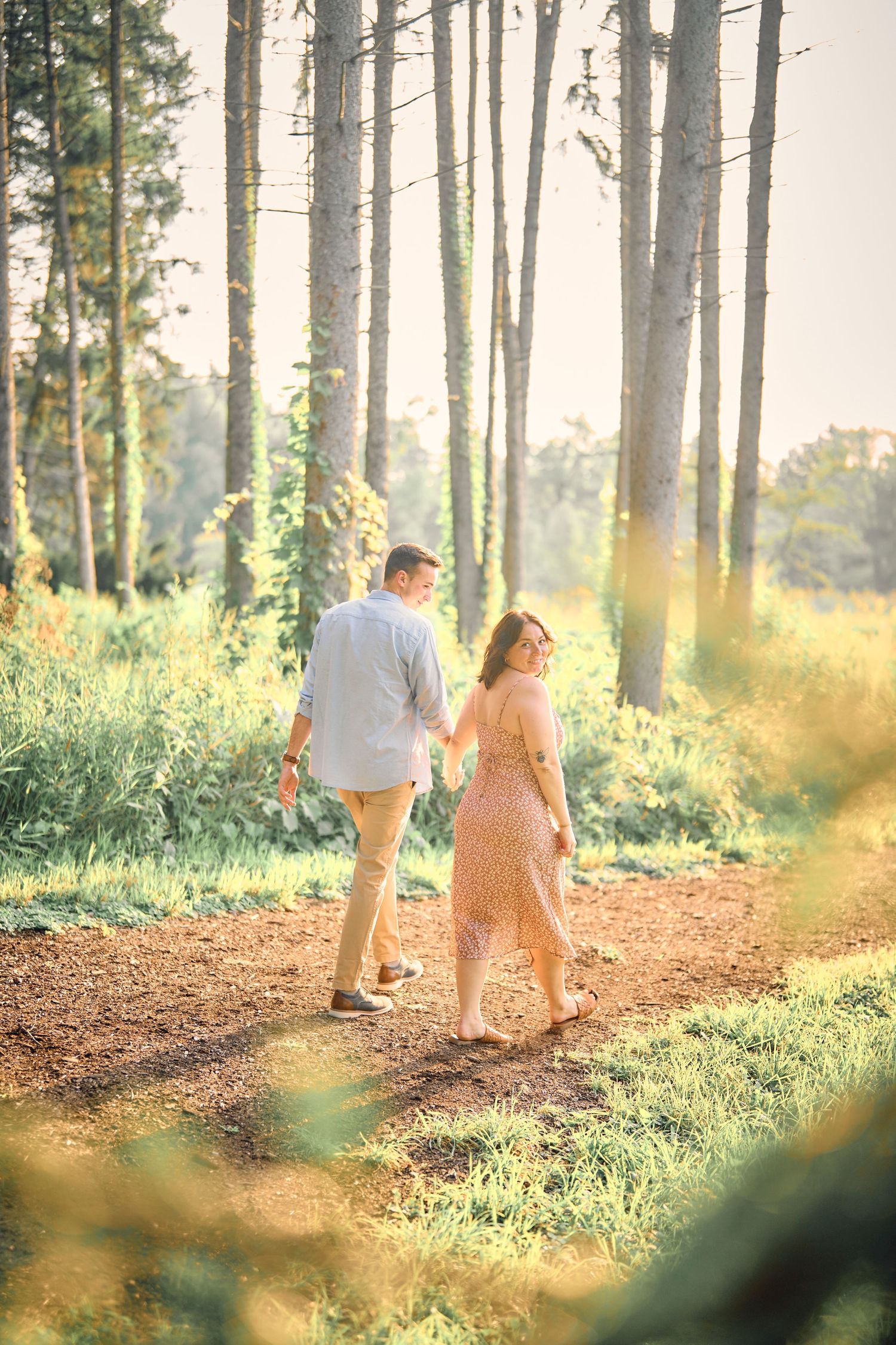 A couple walks hand in hand through a sunlit forest path on a warm summer evening.