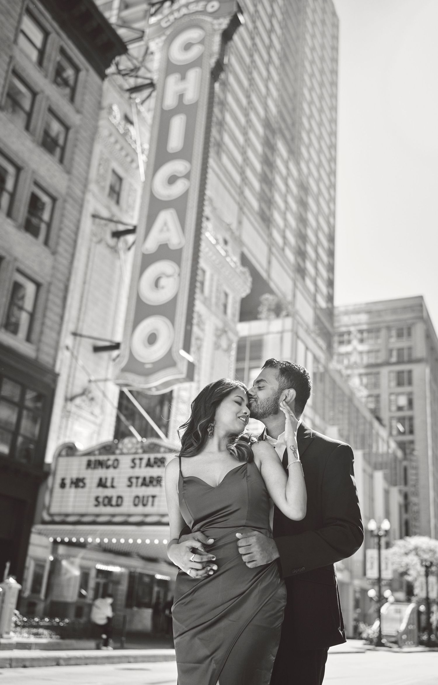 A romantic black and white photo of a couple embracing in front of the historic Chicago Theatre marquee.