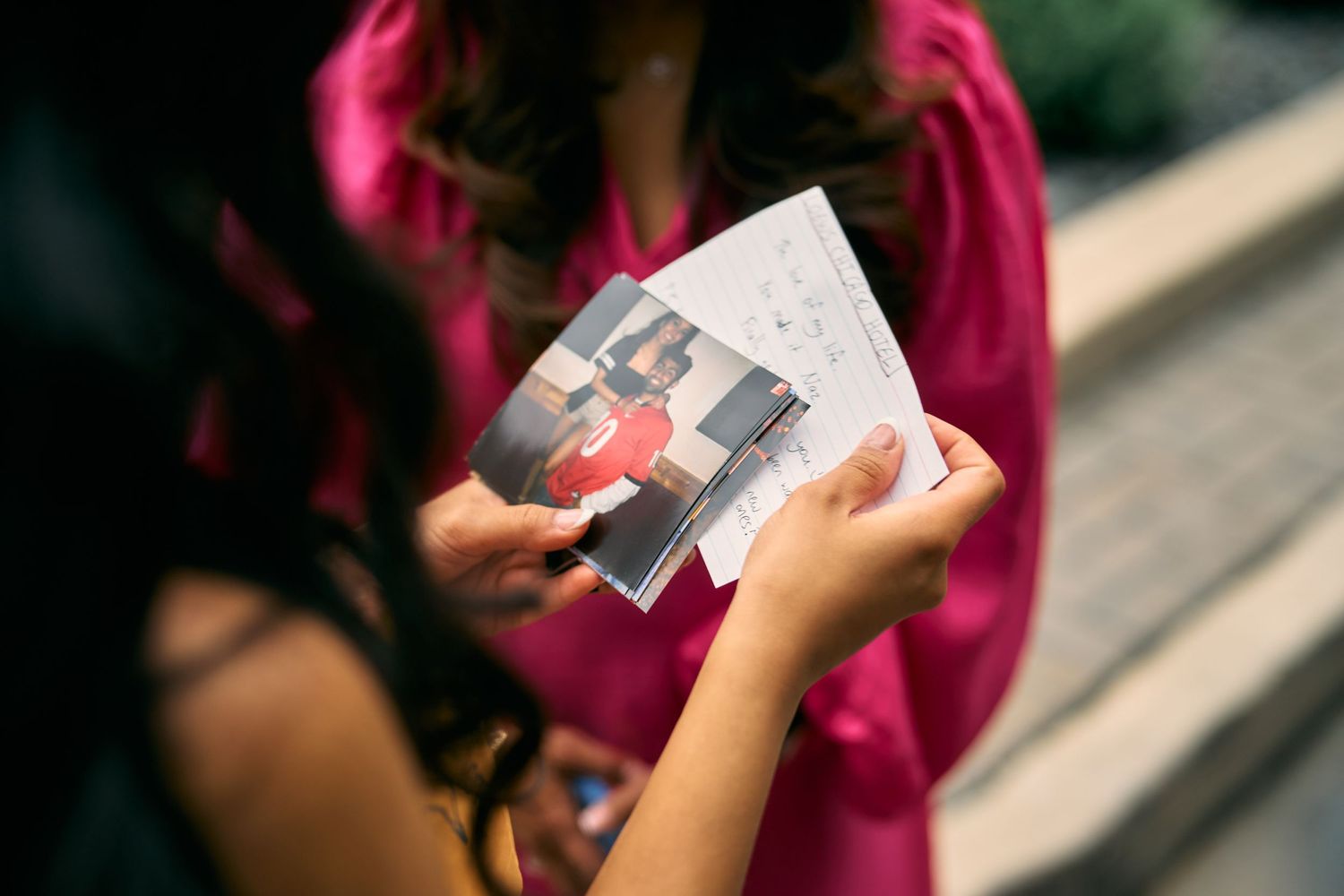 Someone in a pink shirt holds up a printed photograph while looking at it.