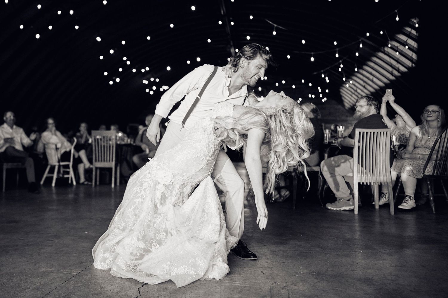 Dramatic wedding dance dip under twinkling lights at outdoor reception.