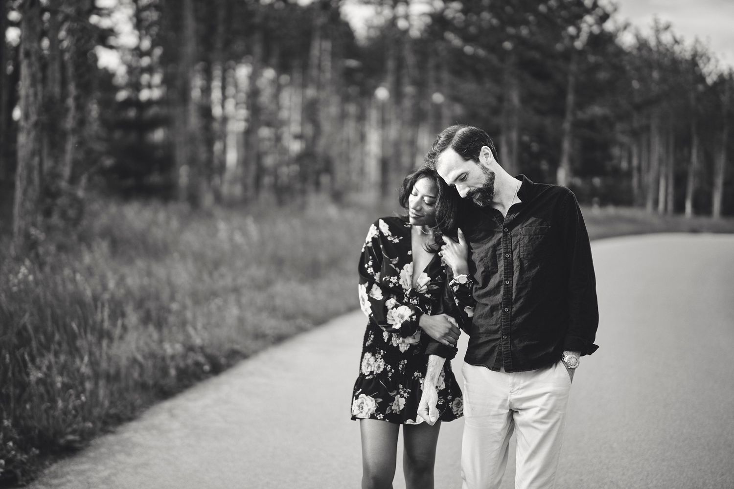 A couple shares an intimate moment together on a tree-lined path in black and white photography.