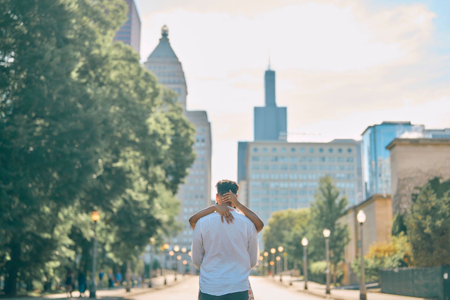 Person in white t-shirt walking down urban street with Chicago skyline and Willis Tower visible in background.