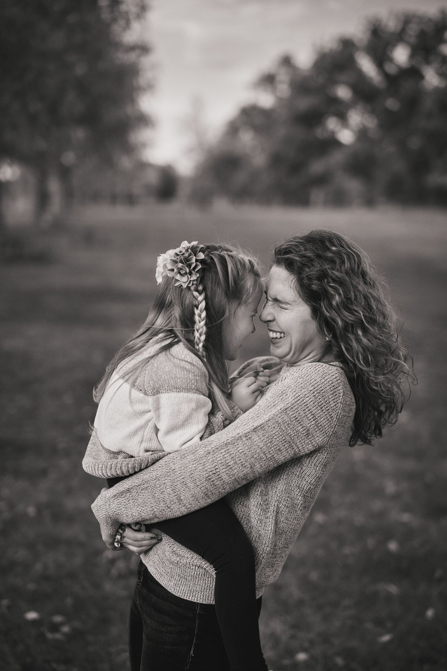 A heartwarming black and white photograph capturing a tender moment of laughter and embrace outdoors in a park setting.