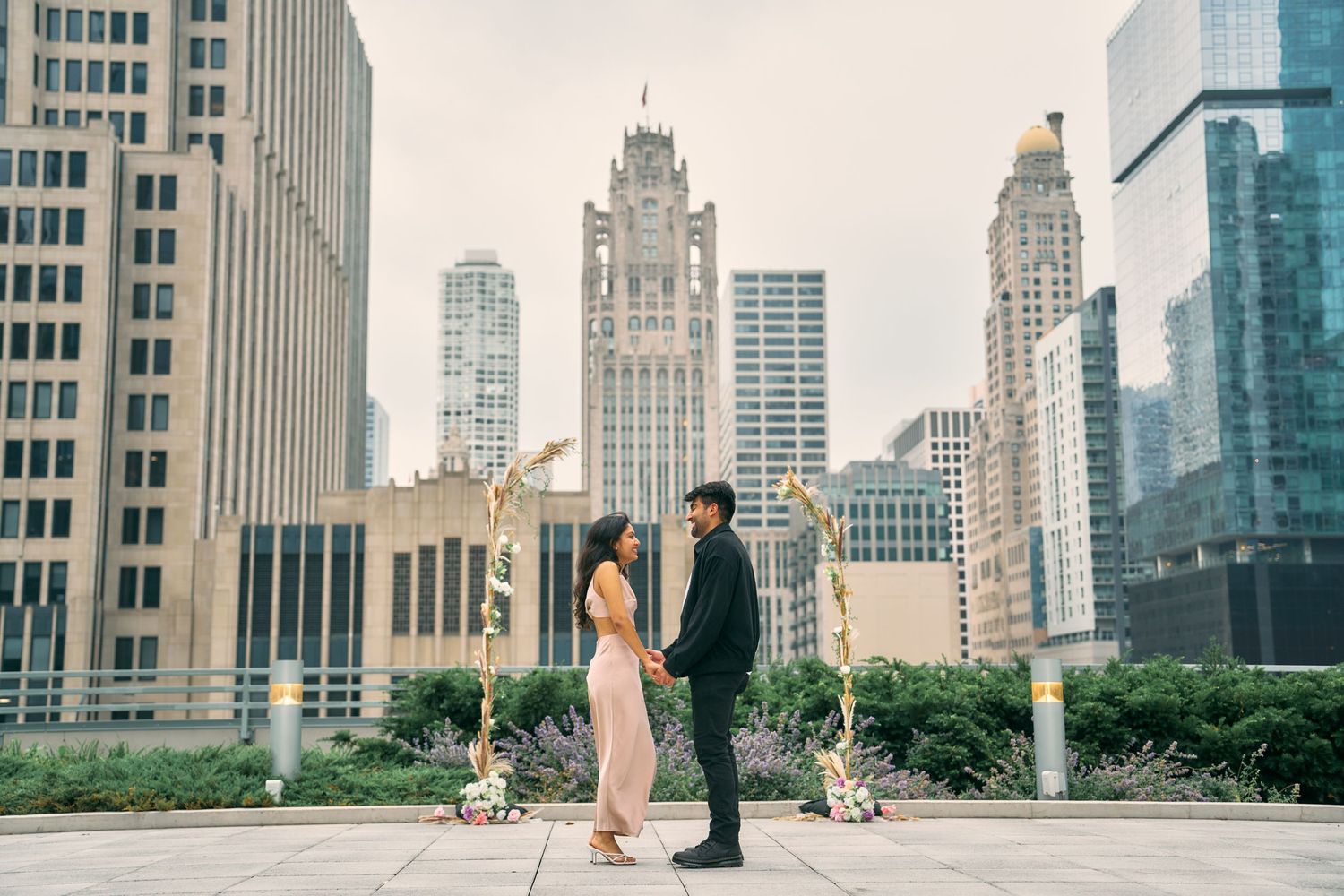 Two people stand with their dogs on an urban walkway with iconic Chicago skyscrapers rising in the background.