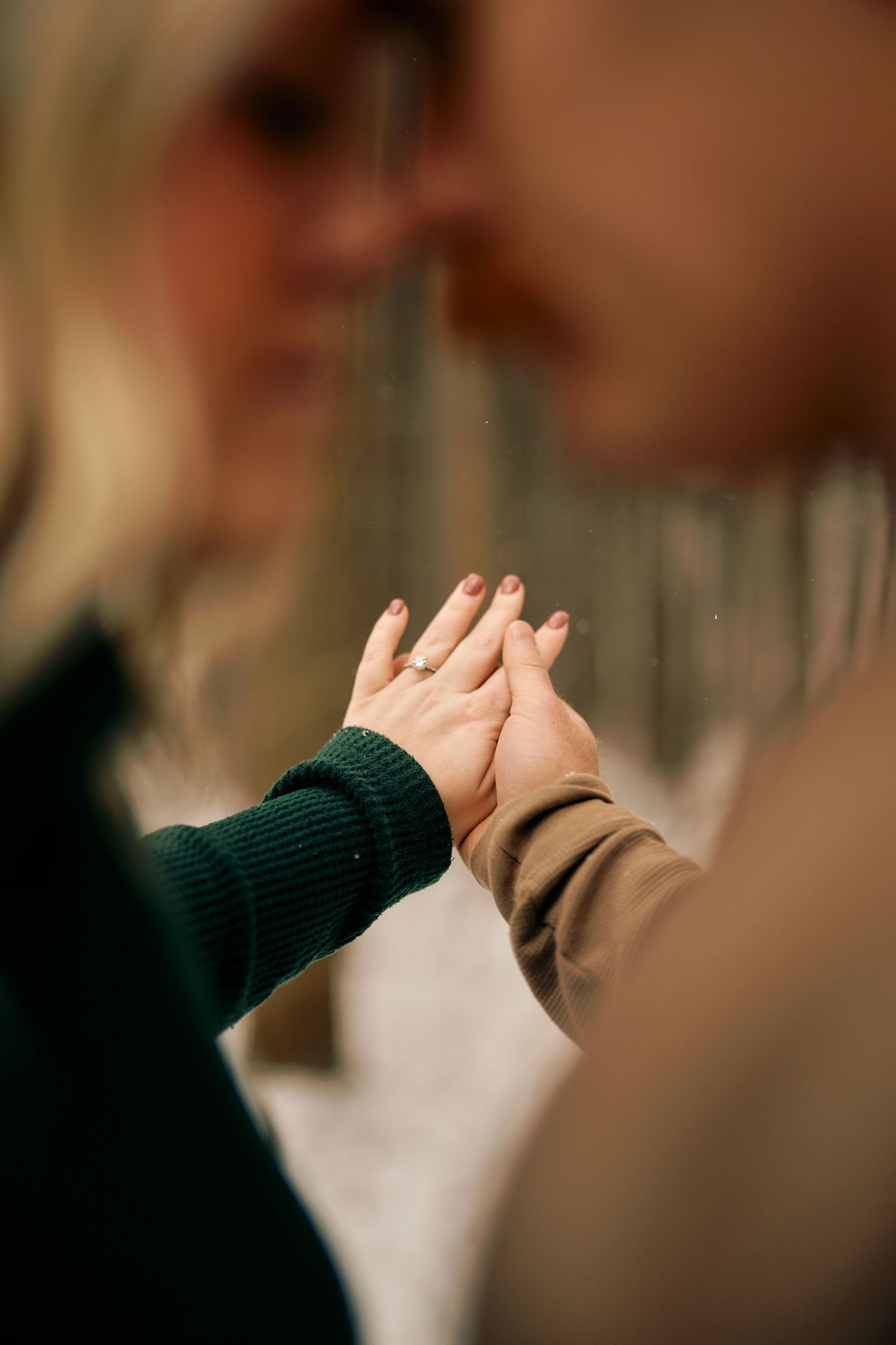 Two people press their palms together in an intimate high-five gesture wearing dark green and brown sweaters.