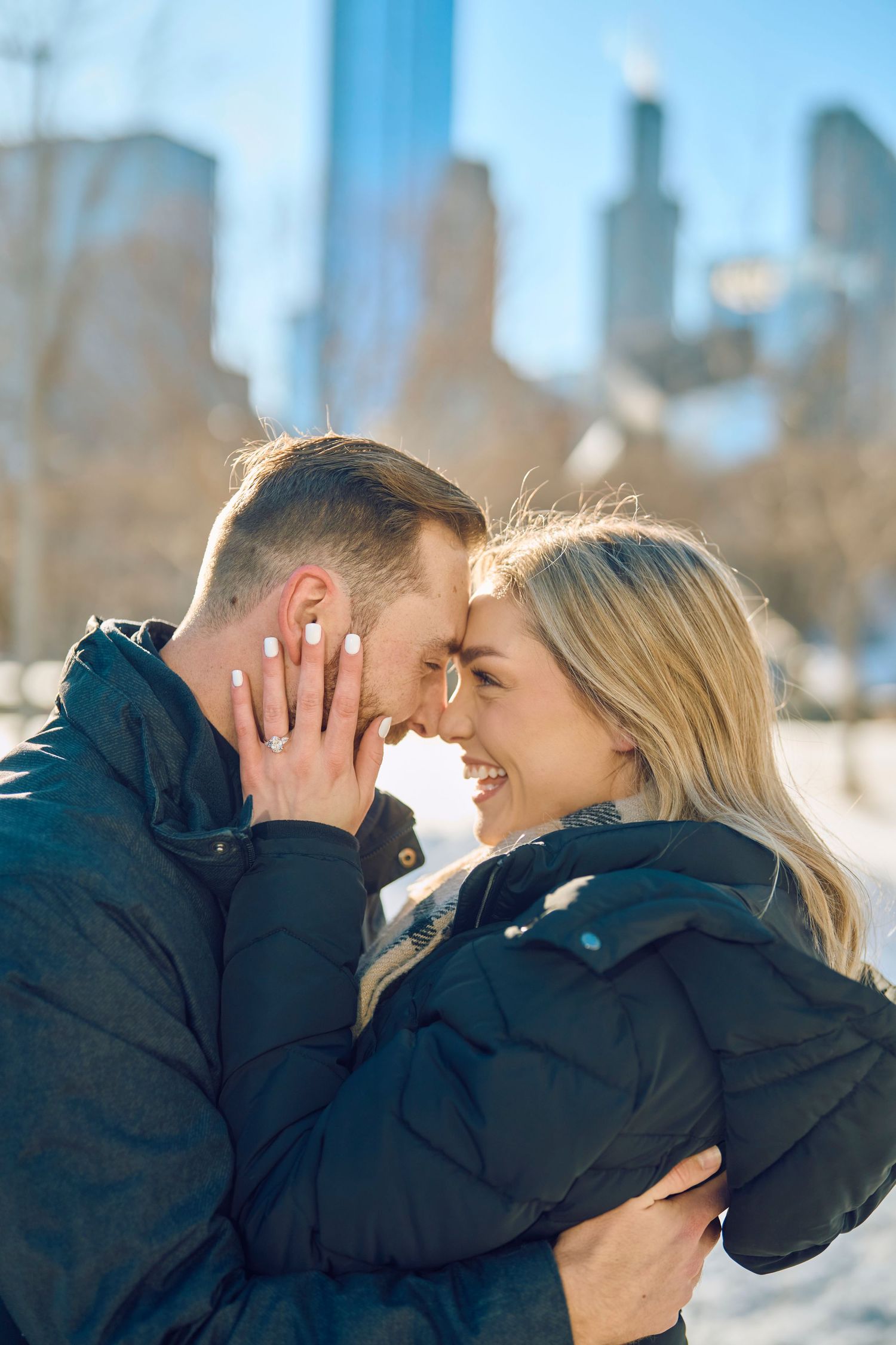 Two people share an intimate moment embracing outdoors with city buildings in the background on a sunny winter day.