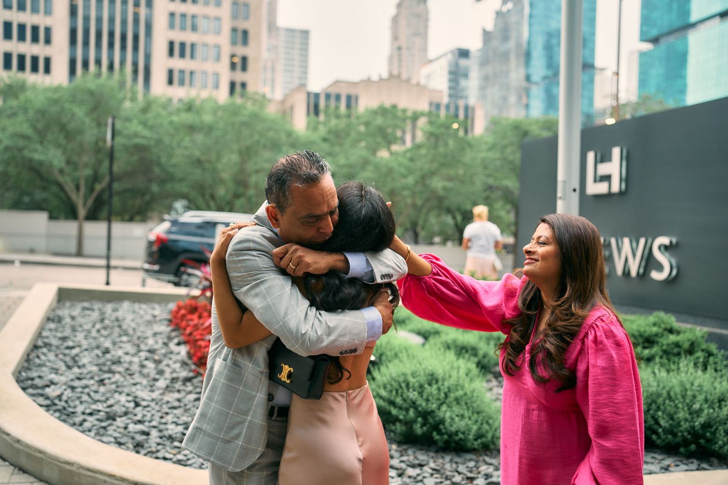 Three people sharing joyful moments together on an urban sidewalk with city buildings in the background.