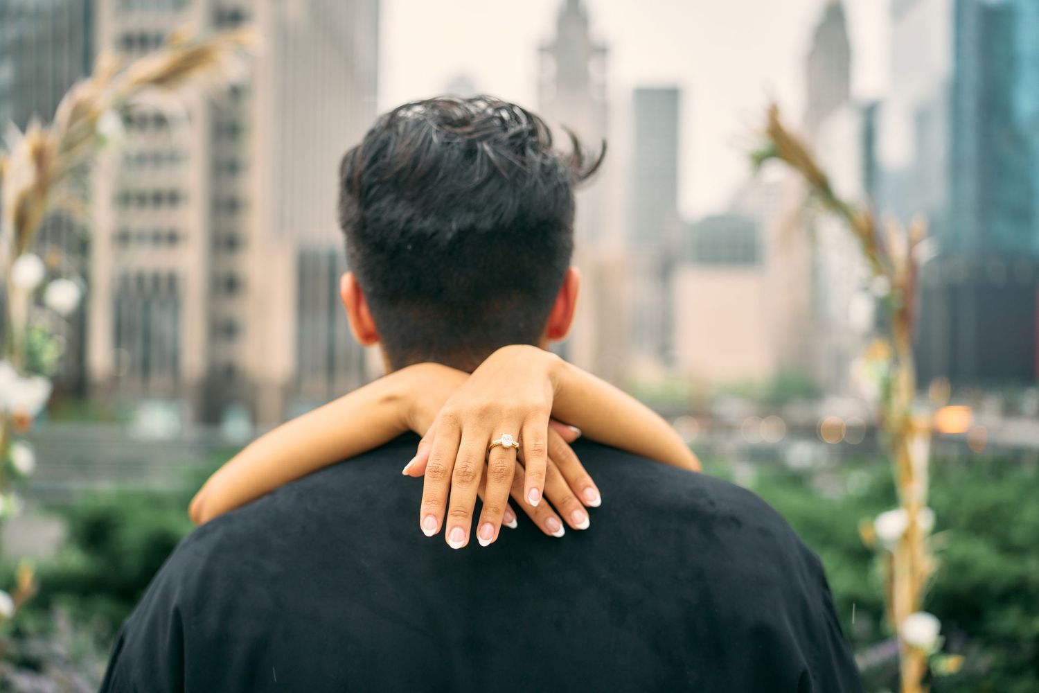 Person in dark shirt viewed from behind with arms wrapped around their neck against city skyline backdrop.