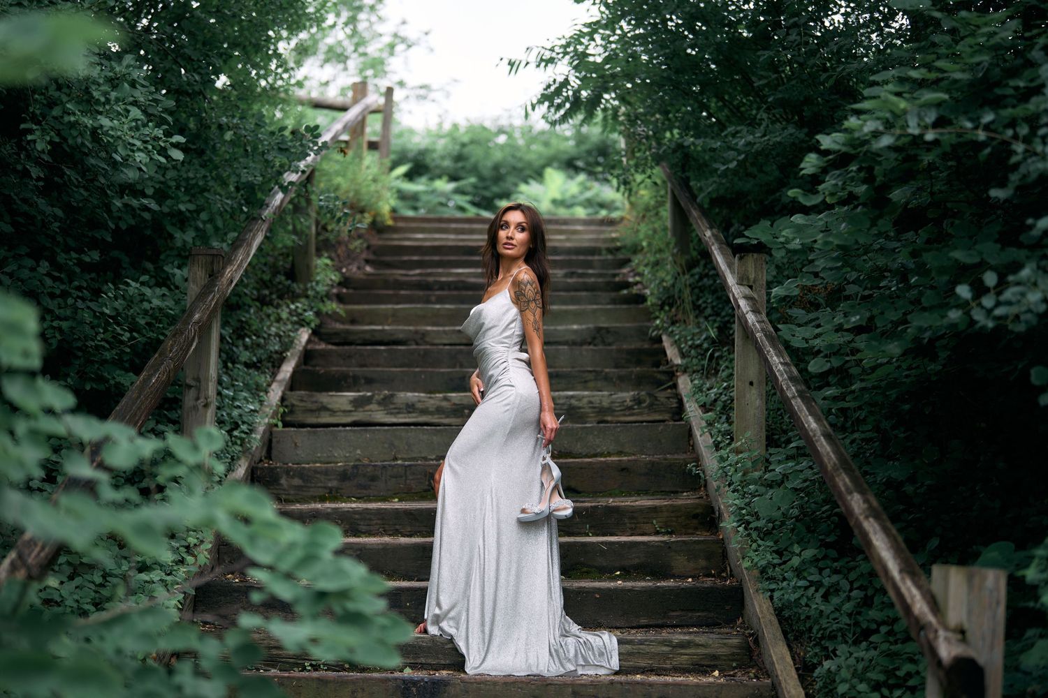 A flowing white dress cascades down wooden stairs surrounded by lush greenery.