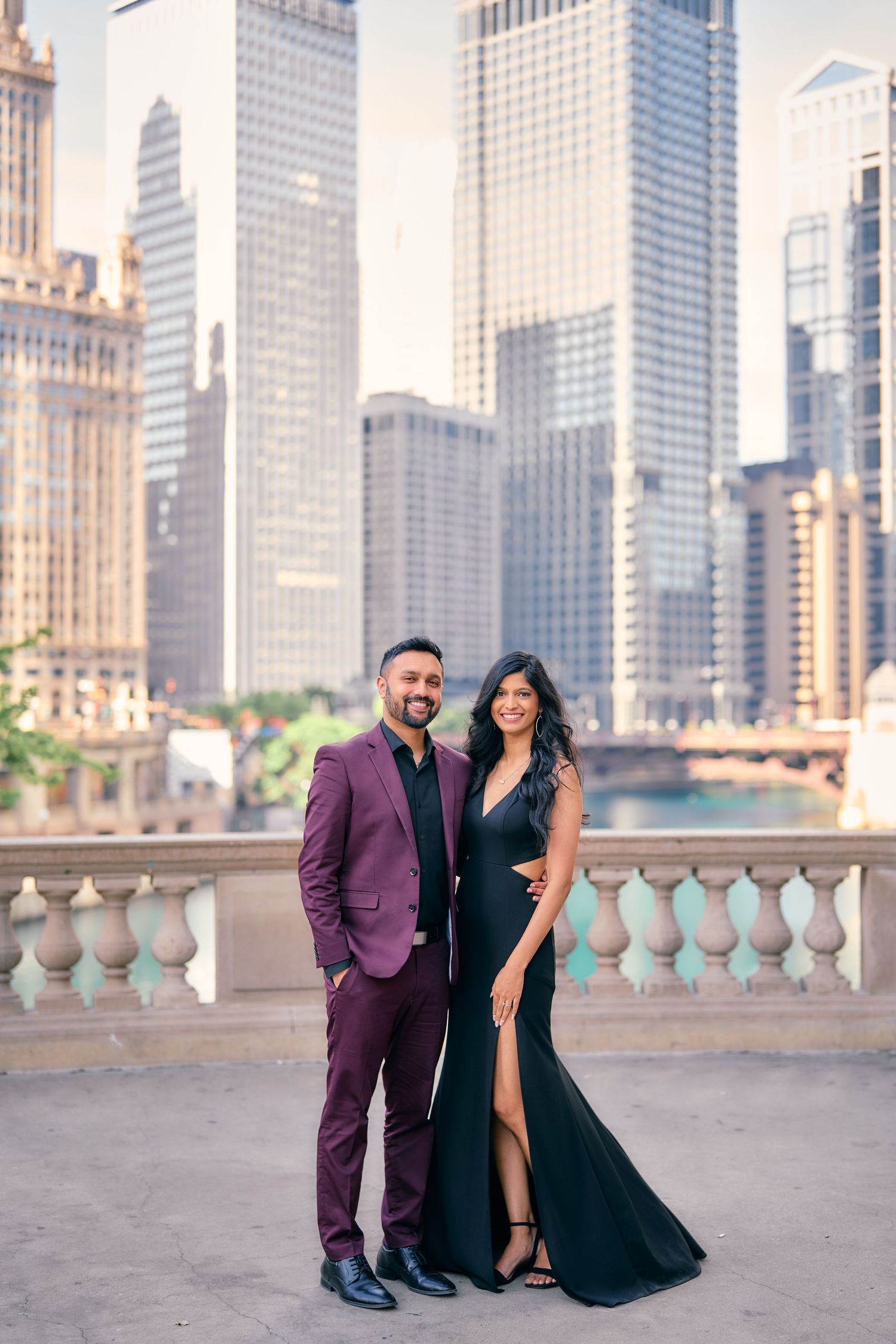Elegant couple poses on stone balcony overlooking Chicago skyline with modern skyscrapers in background.