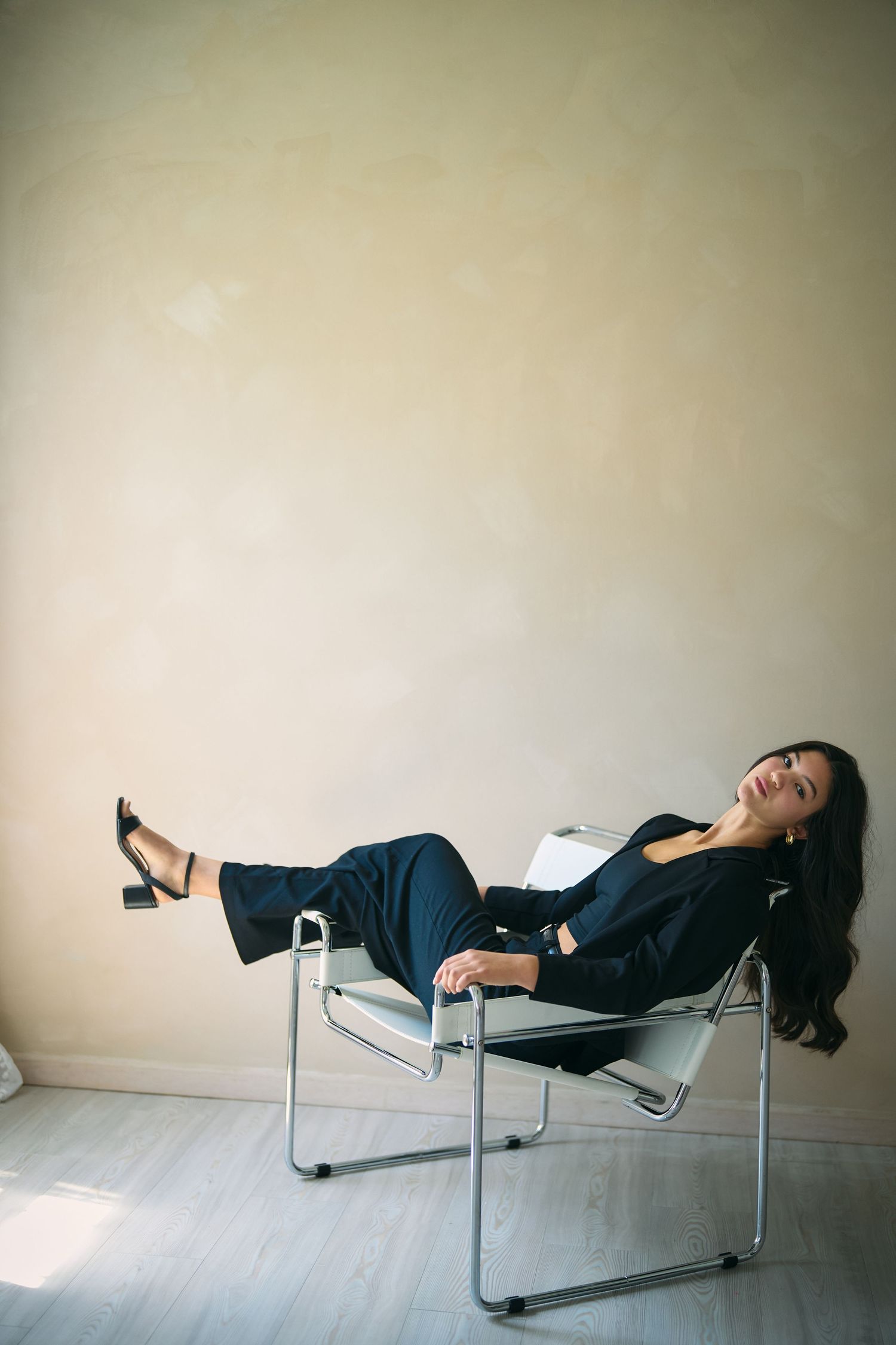 A series of five photos showing someone reclining on a minimalist chrome lounge chair against a white wall.