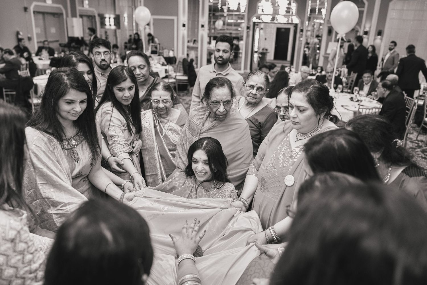 A group in matching satin robes gather around in a circle at an indoor celebration venue.