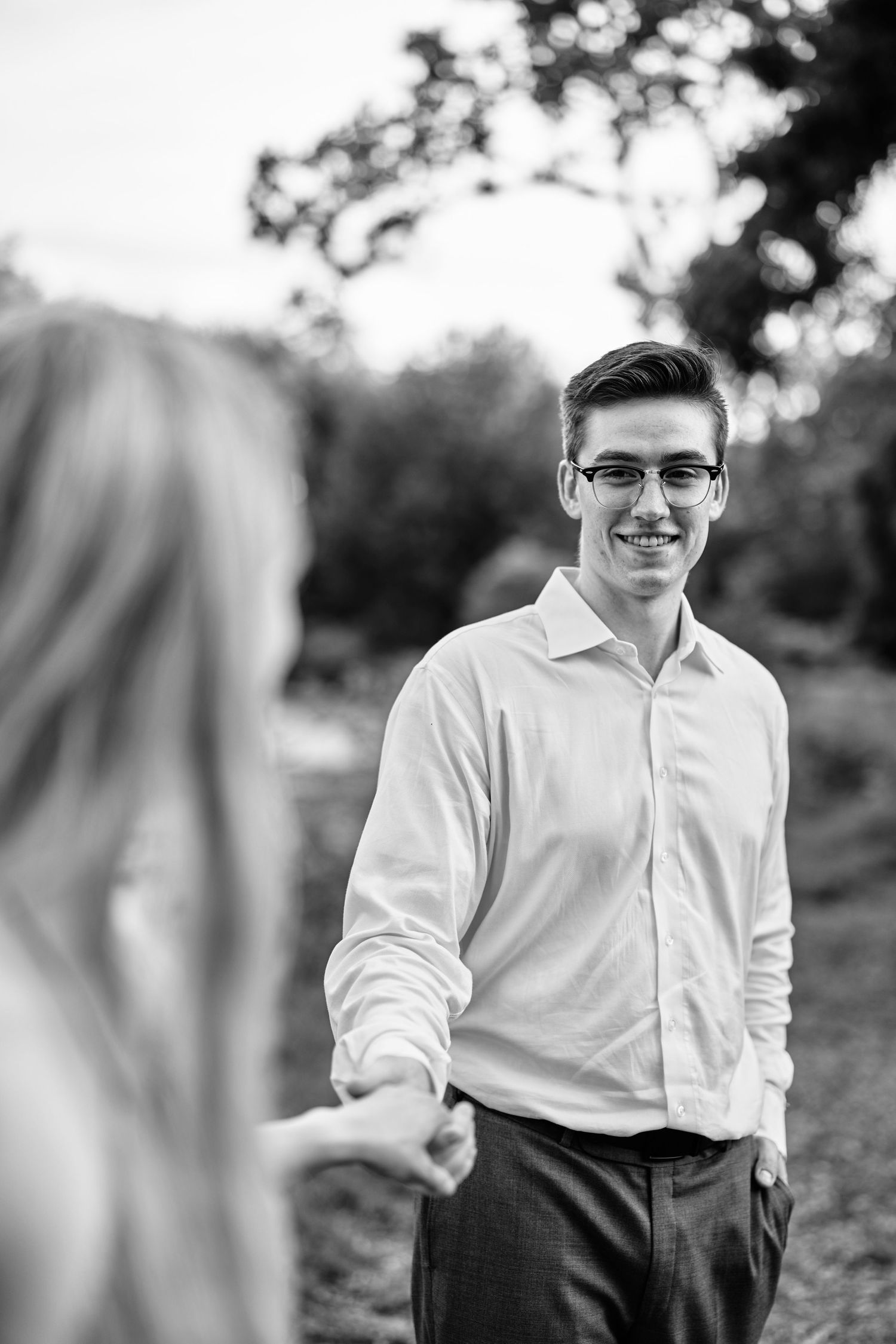 A candid black and white portrait of a person smiling warmly outdoors on a sunny day.
