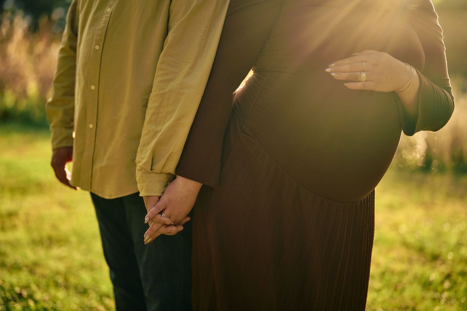 Romantic couple embraces in a golden sunlit field during sunset creating a dreamy silhouette effect.