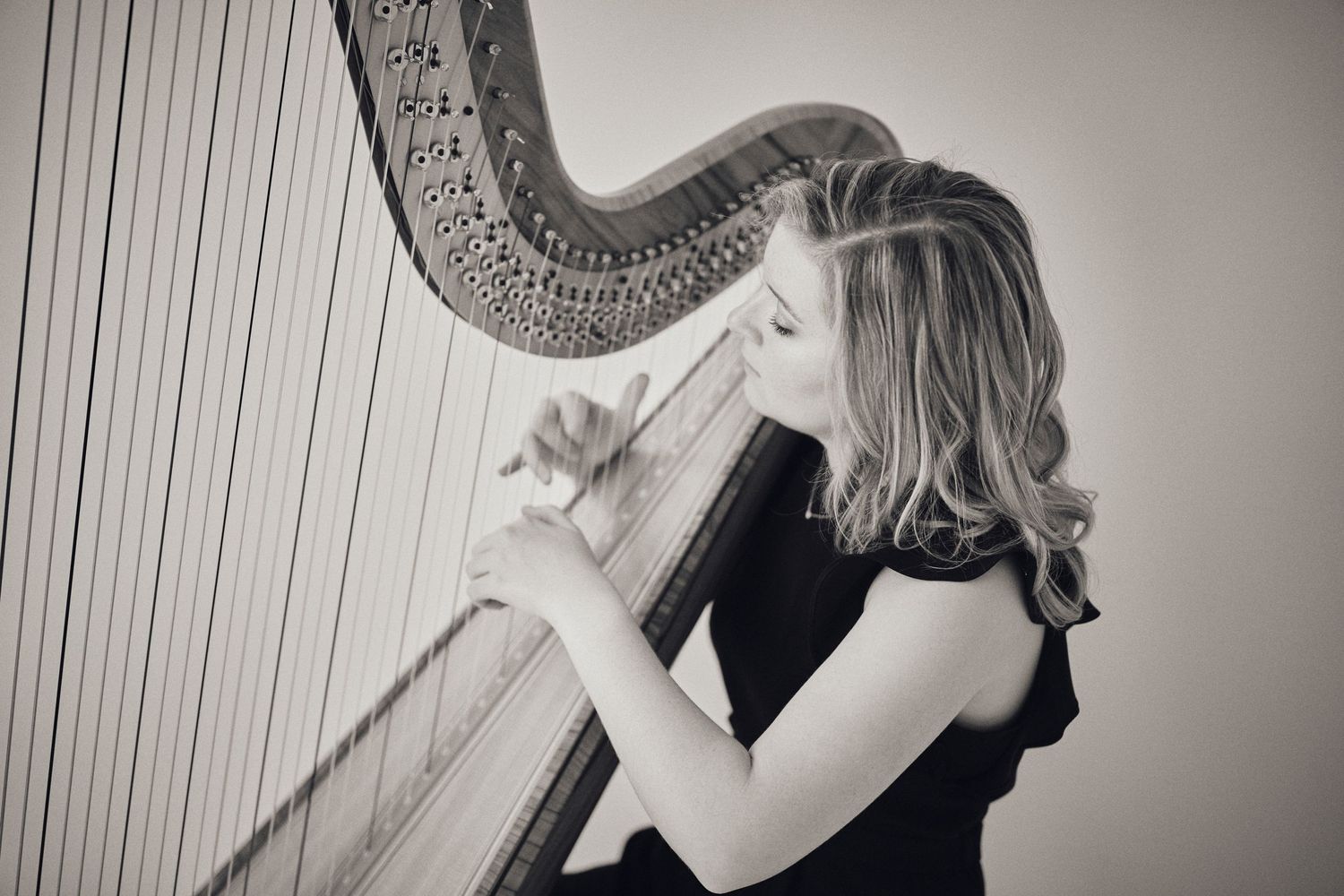 Black and white artistic photo of musician playing classical harp with dramatic lighting.