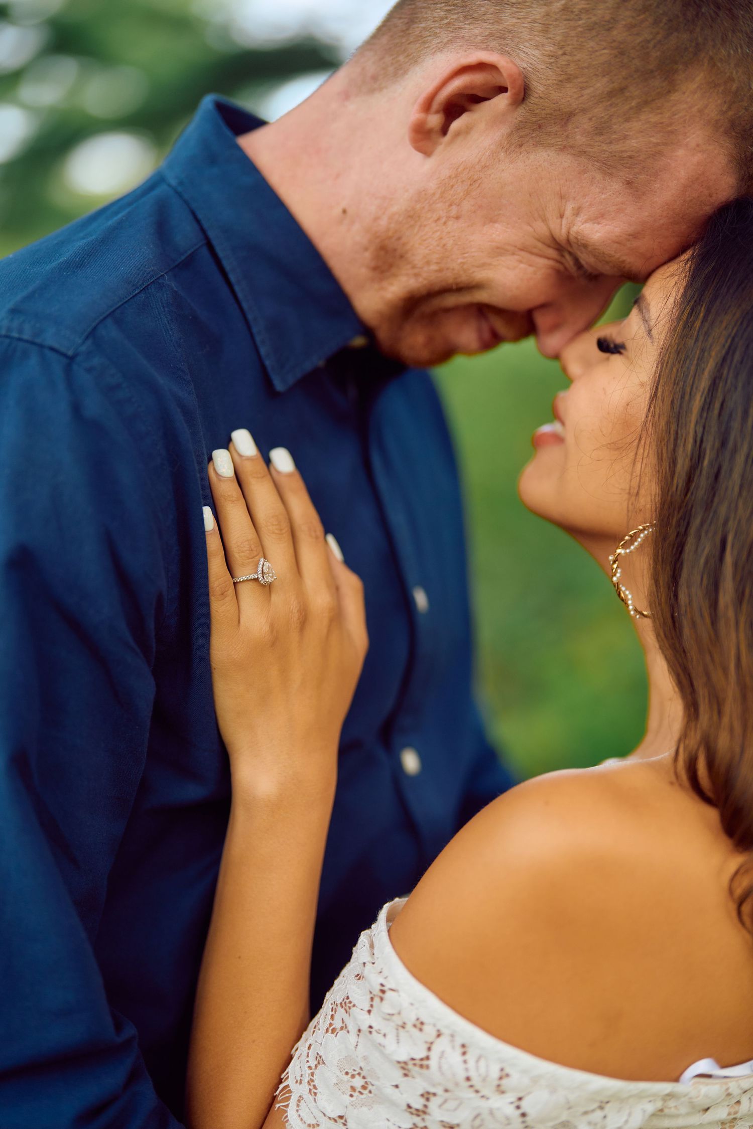 A romantic engagement photo showing a couple in an intimate moment, with her diamond ring visible against his navy shirt.