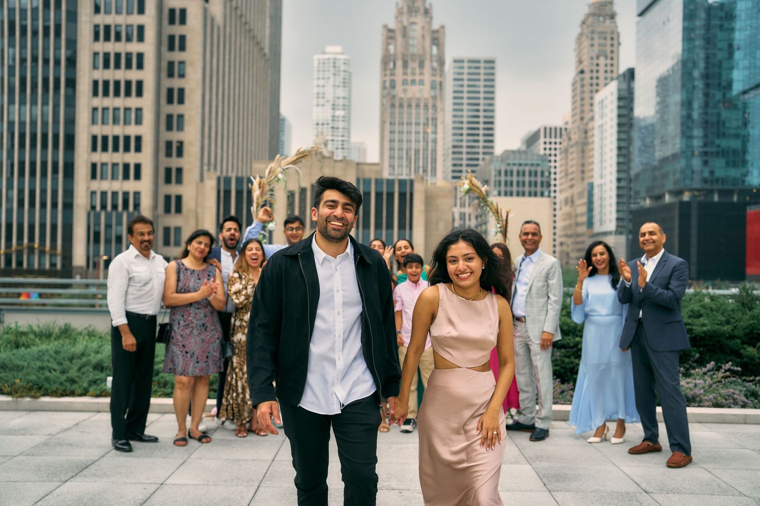 A couple walks together on the Riverwalk in downtown Chicago with the iconic skyline and other people in the background.