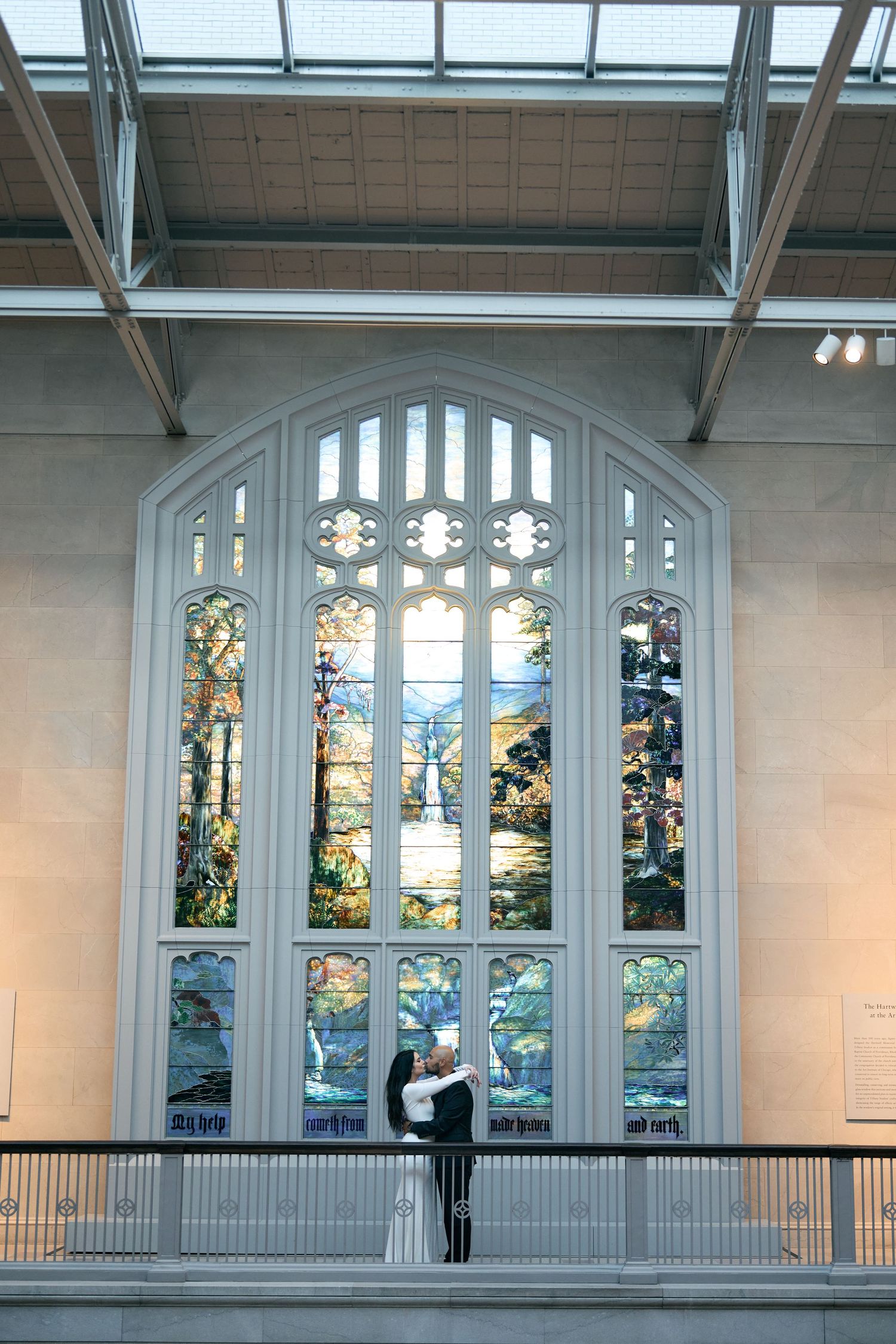 A figure stands silhouetted against a towering stained glass church window with ornate religious artwork and architectural details.