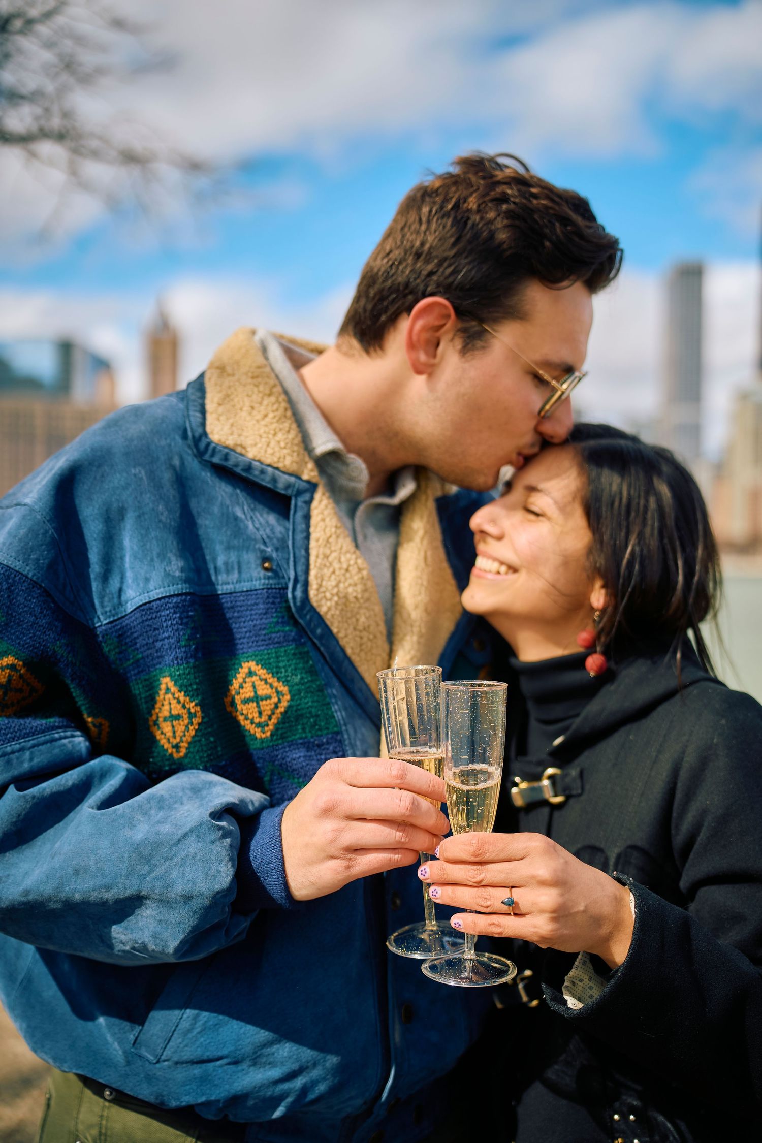 Intimate moment between couple drinking champagne with urban buildings in background.