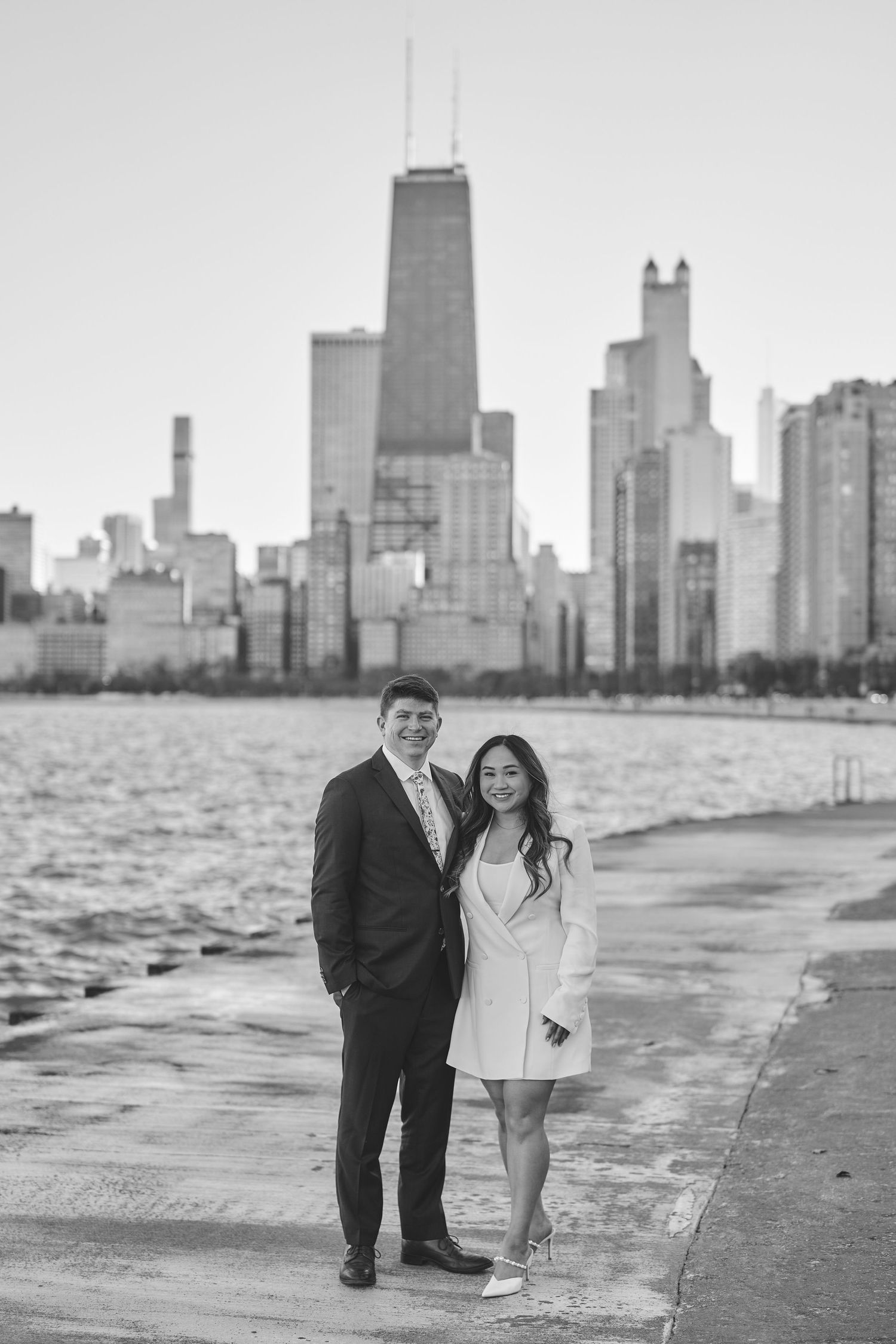 A couple stands together along Chicago's North Avenue Beach with the iconic skyline and John Hancock building in the background.