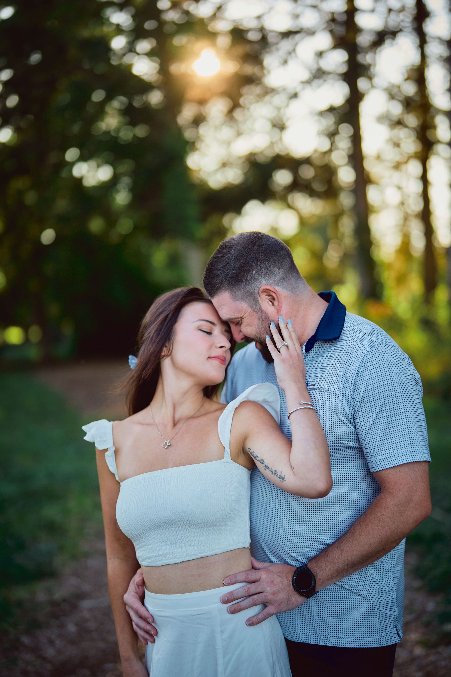 A tender romantic moment between a couple embracing in a sunlit forest during golden hour.