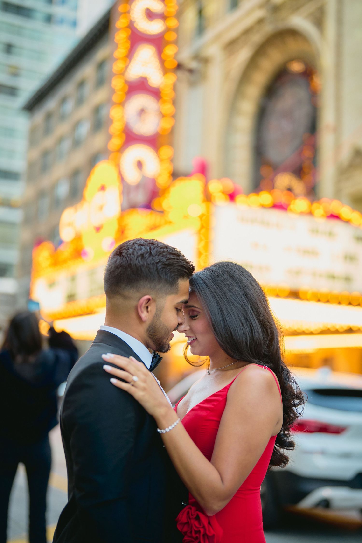 A romantic couple embraces outside the Chicago Theatre with its iconic illuminated marquee glowing in the background.