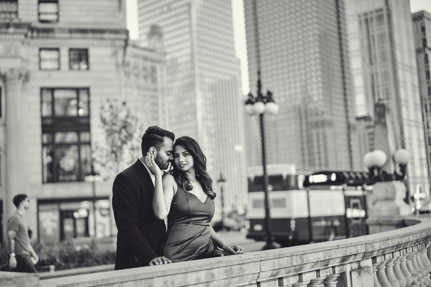 A couple shares a romantic moment on a city balcony with urban buildings and lampposts in the background.