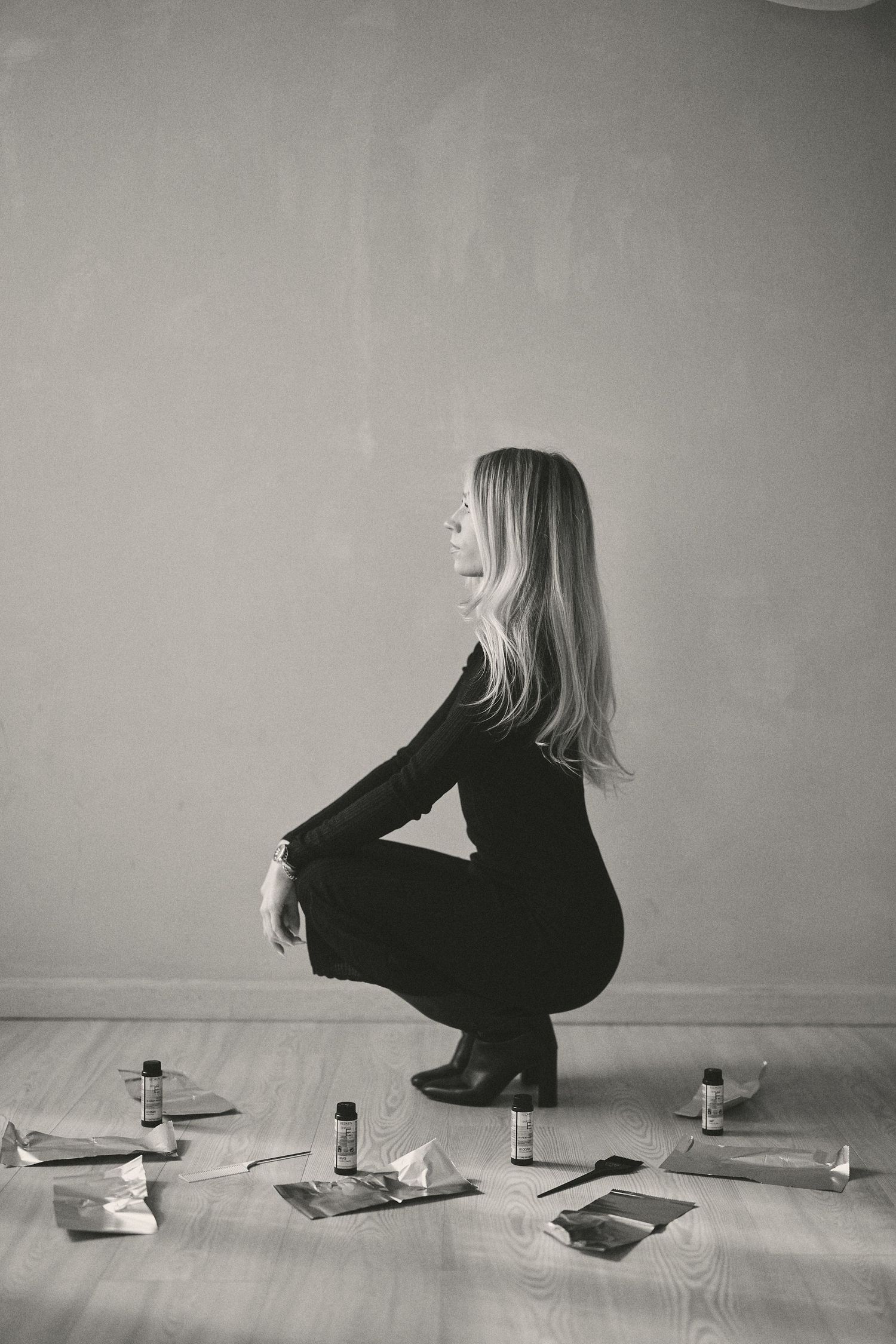 Black and white photo of person in dark clothing crouching near scattered items on wooden floor.