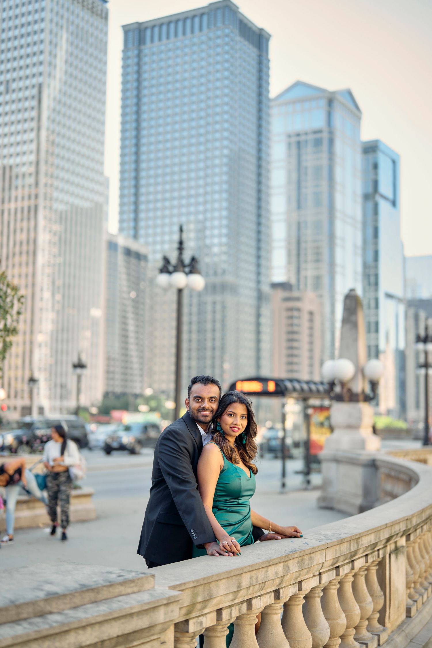A romantic couple poses on a stone balustrade with Chicago's modern skyscrapers forming a dramatic urban backdrop.