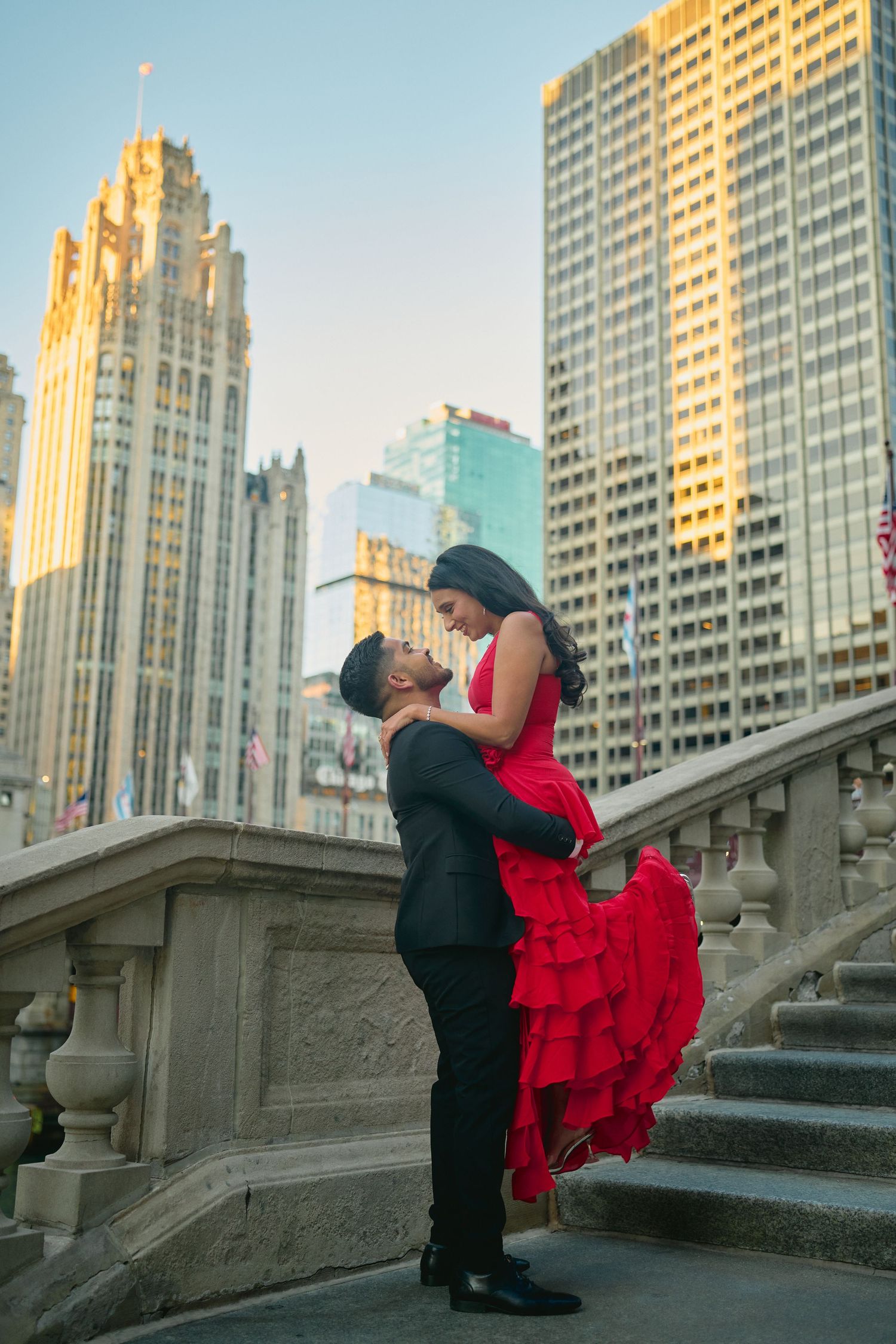 Romantic couple embraces on stone steps with Chicago's iconic Tribune Tower and skyscrapers during golden hour.