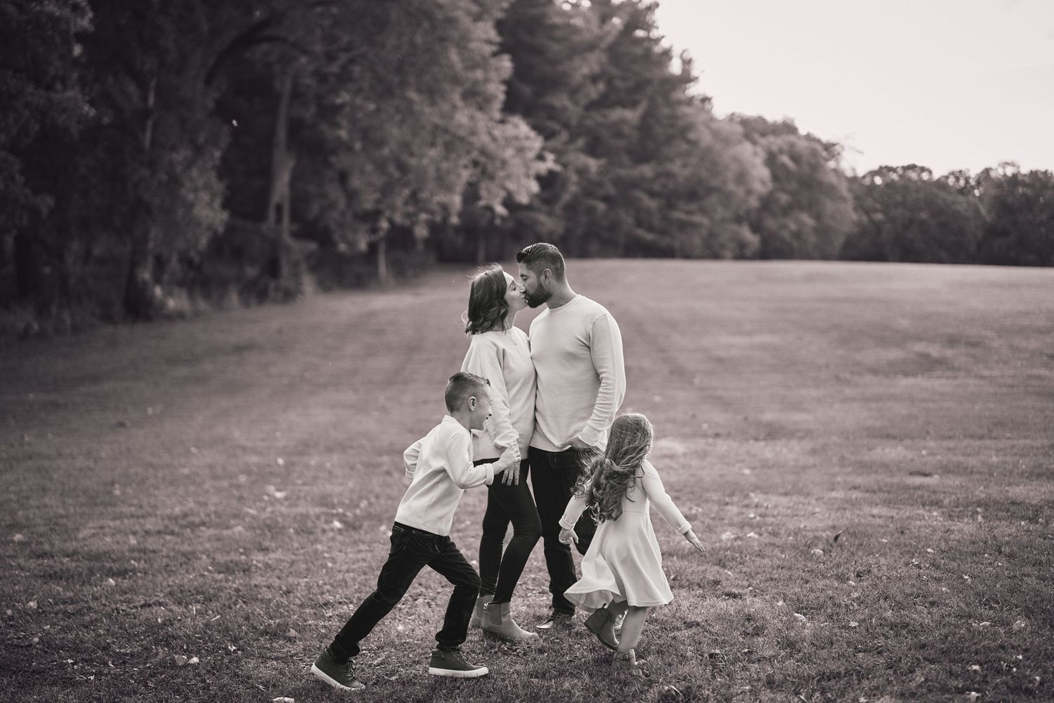 A couple shares a tender moment with their child while playing together in a grassy field on a summer day.